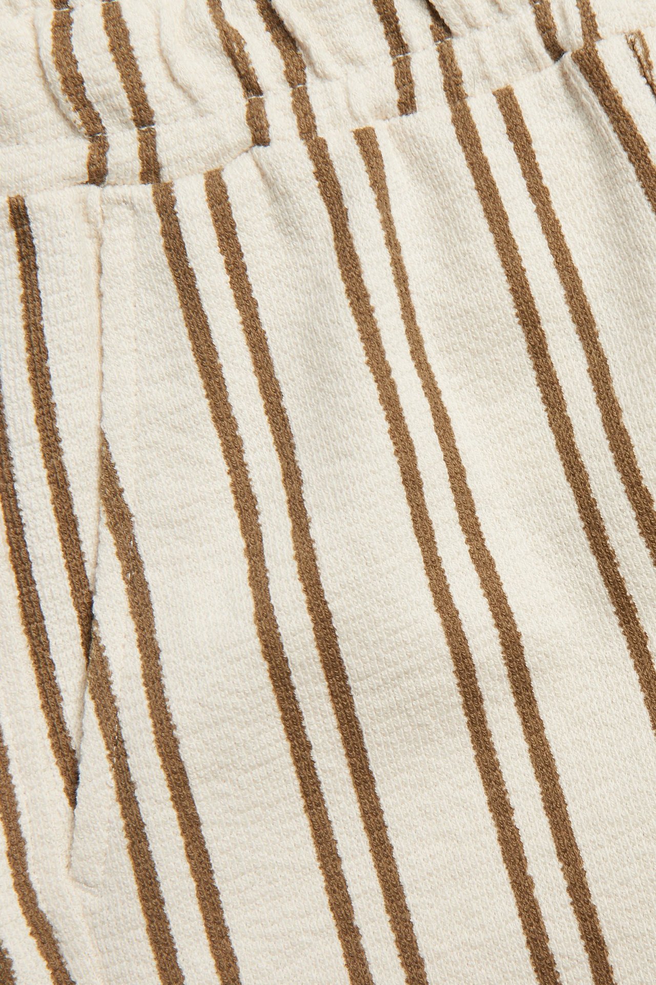 Närbild av ljusbeige randiga shorts i bomullsjersey med resår i midjan och fickor.