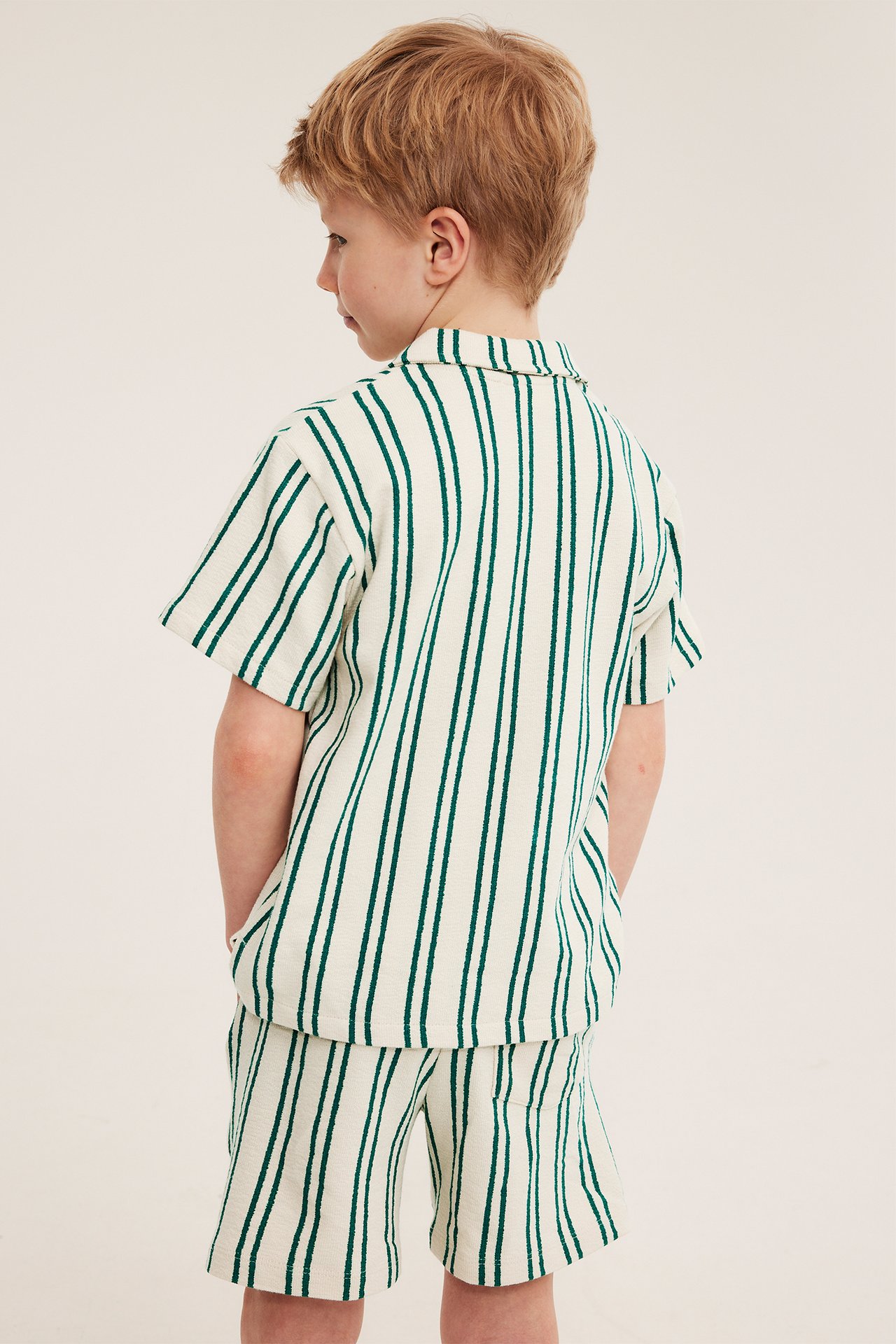 Bakifrån: Barn bär off-white och grönt randvävda mjukisshorts med matchande kortärmad topp.
