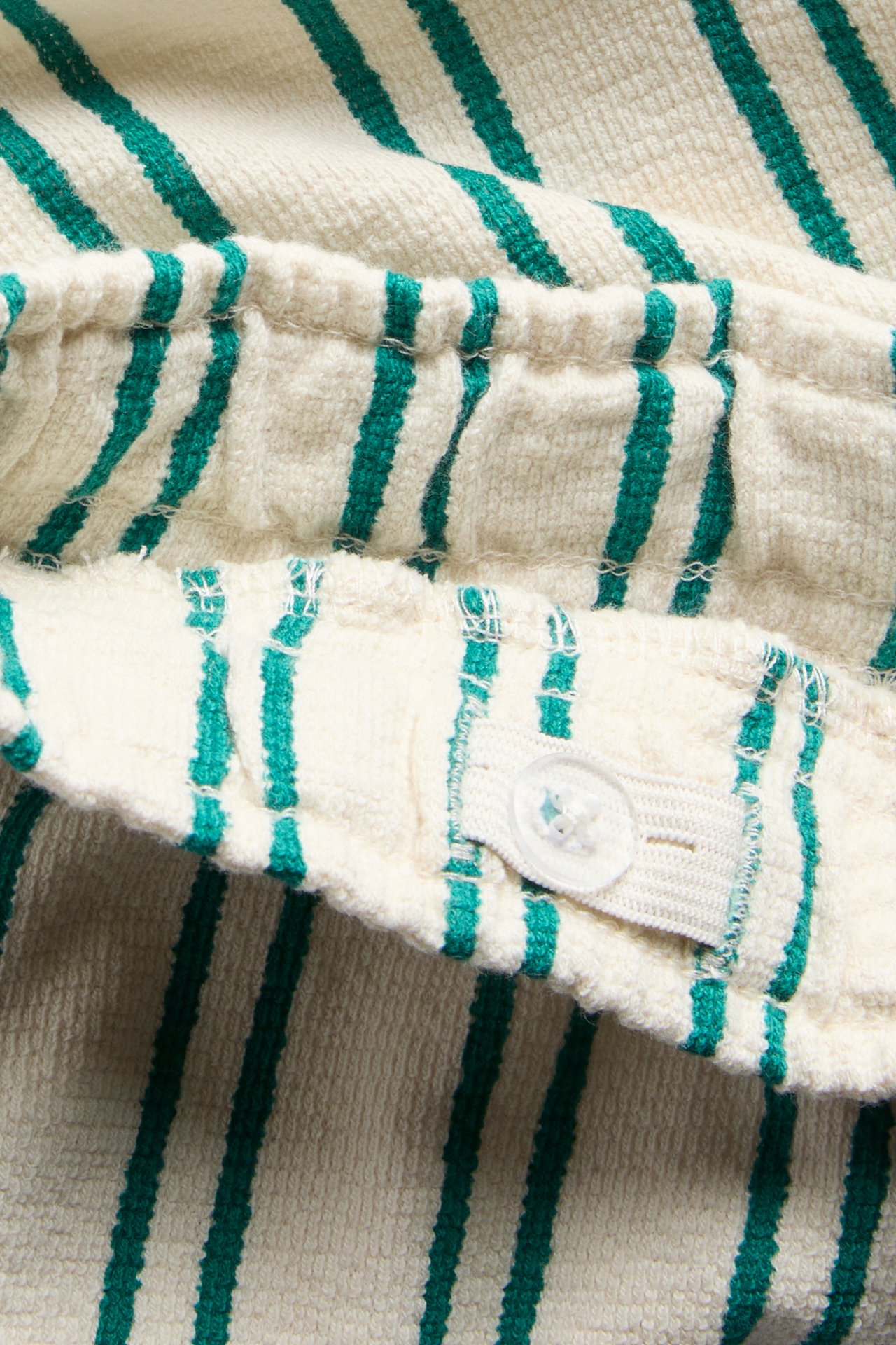 Zbliżenie na zielono-kremowe, pasiaste miękkie bawełniane szorty z regulowanym pasem na guzik.