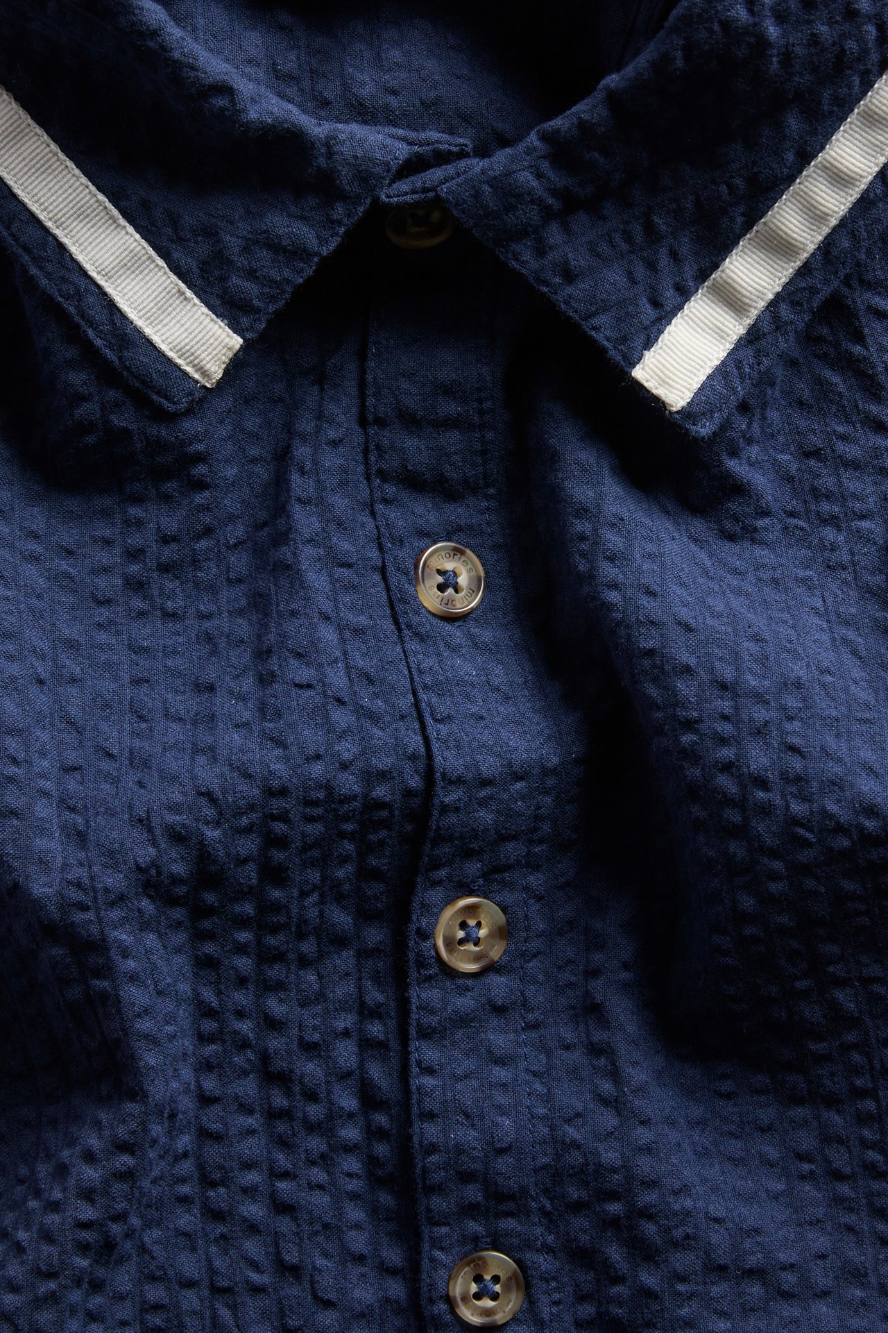 Lähikuva edestä sinisestä seersucker-romperista, jossa raidallinen kaulus ja etunapit.