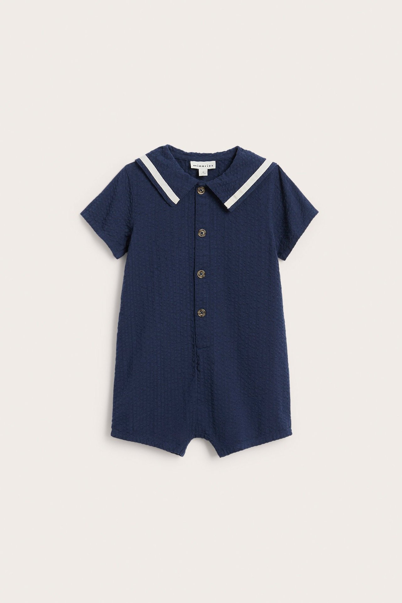 Framsida av mörkblå babyromper i seersuckerbomull med vitrandig sjömanskrage och knappar framtill.