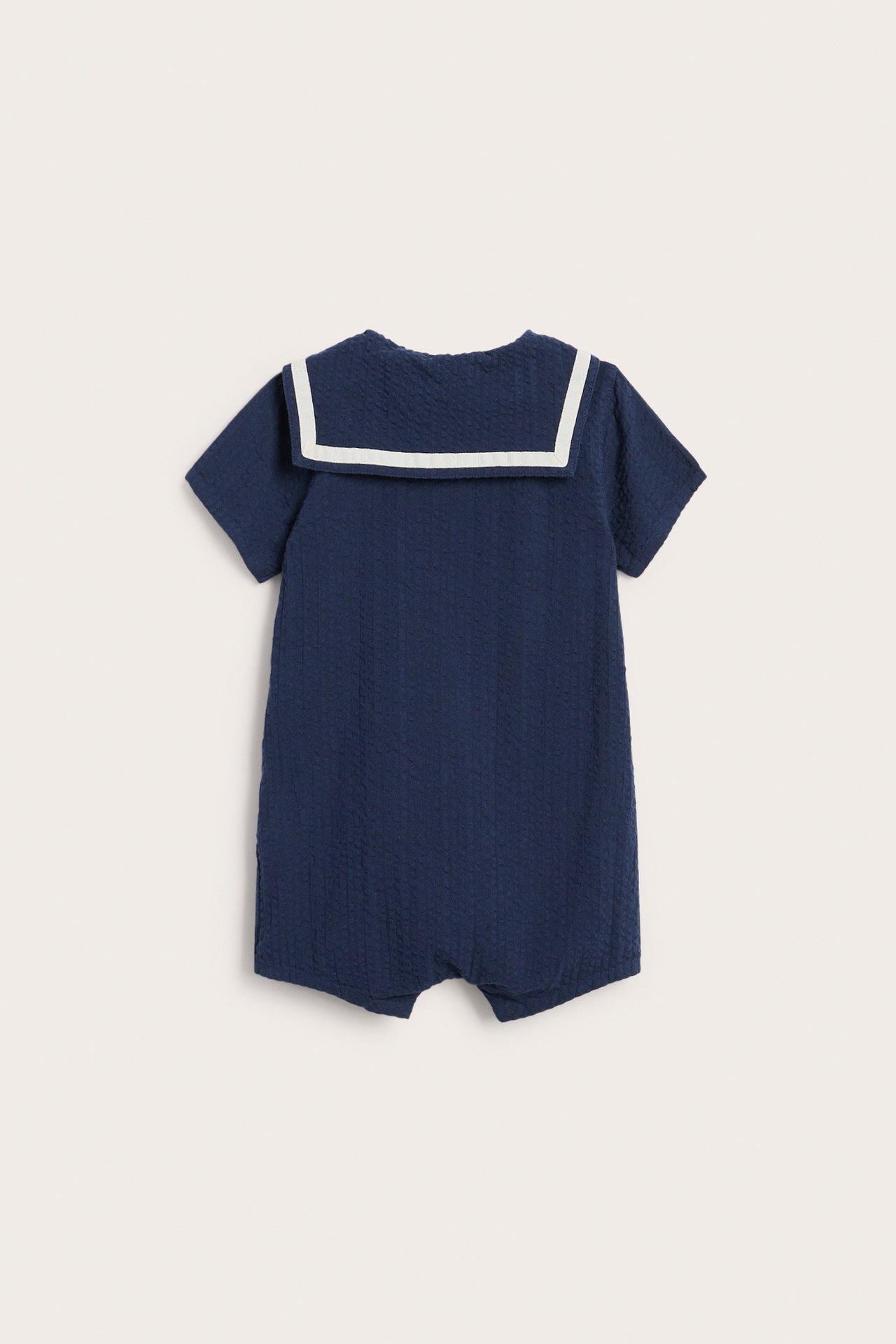 Takaapäin kuvattu laivastonsininen puuvillainen vauvanhaalari, lyhyet hihat ja valkoinen merimieskaulus.