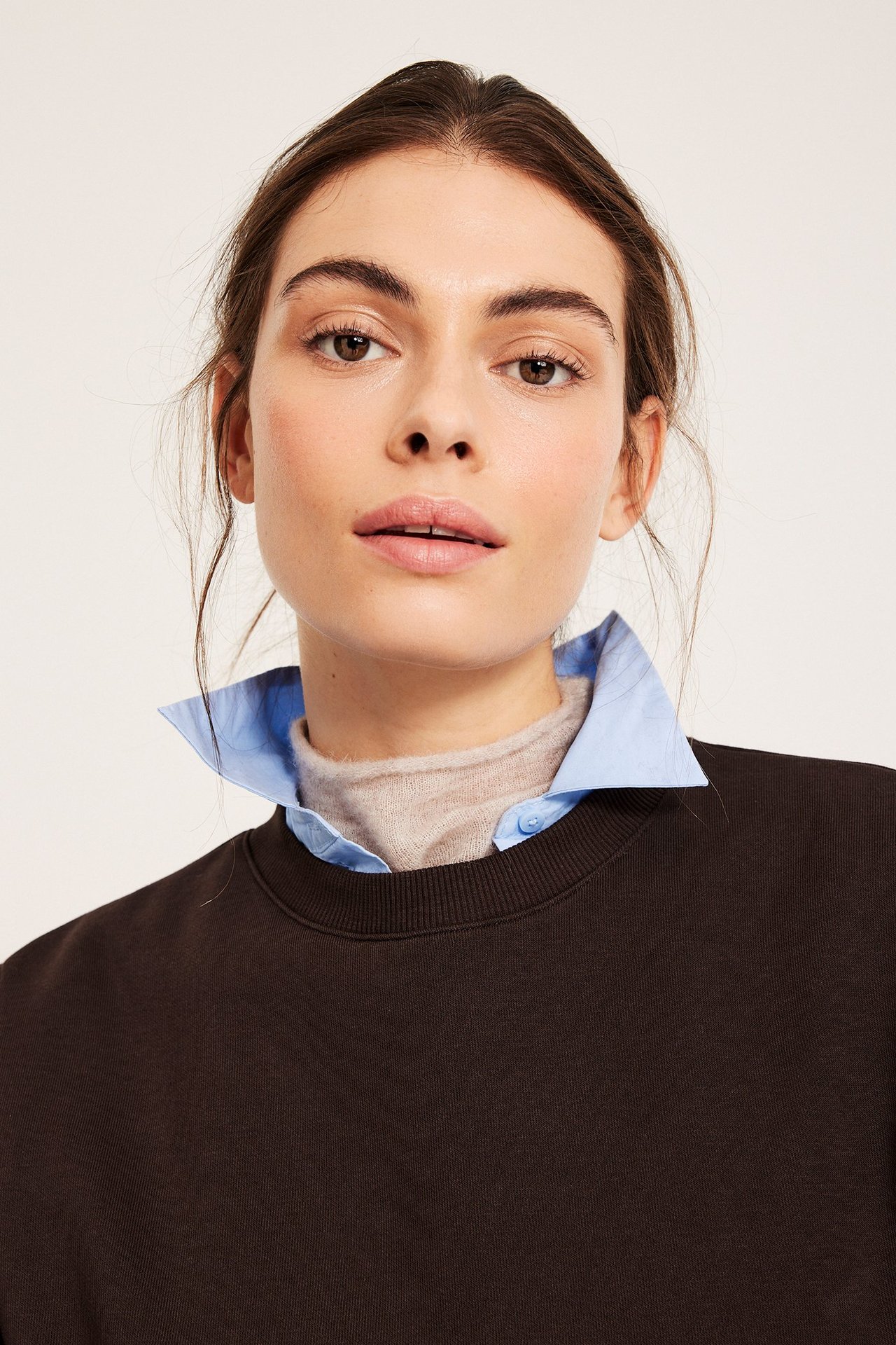 Lähikuva naisesta tummanruskeassa collegepaidassa vaaleansinisen kauluspaidan ja beigen poolopaidan päällä.