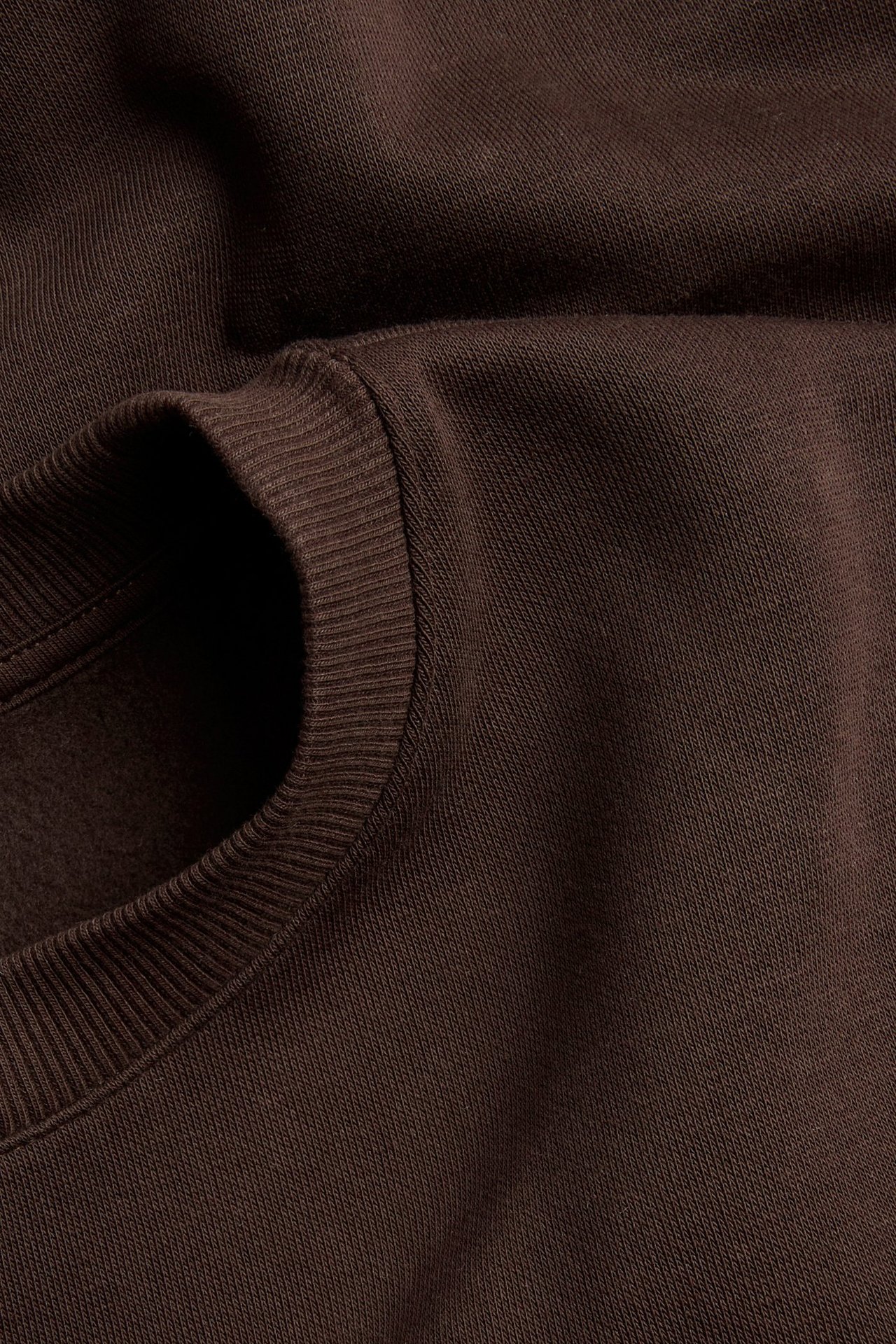 Zbliżenie na gładką, ciemnobrązową bluzę dresową z prążkowanym okrągłym dekoltem i mankietami.
