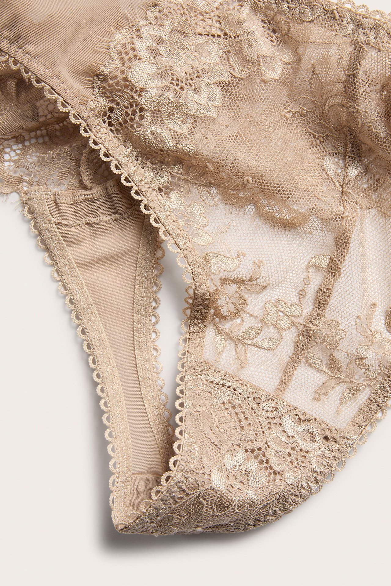 Zbliżenie beżowych koronkowych stringów z kwiatowymi detalami.