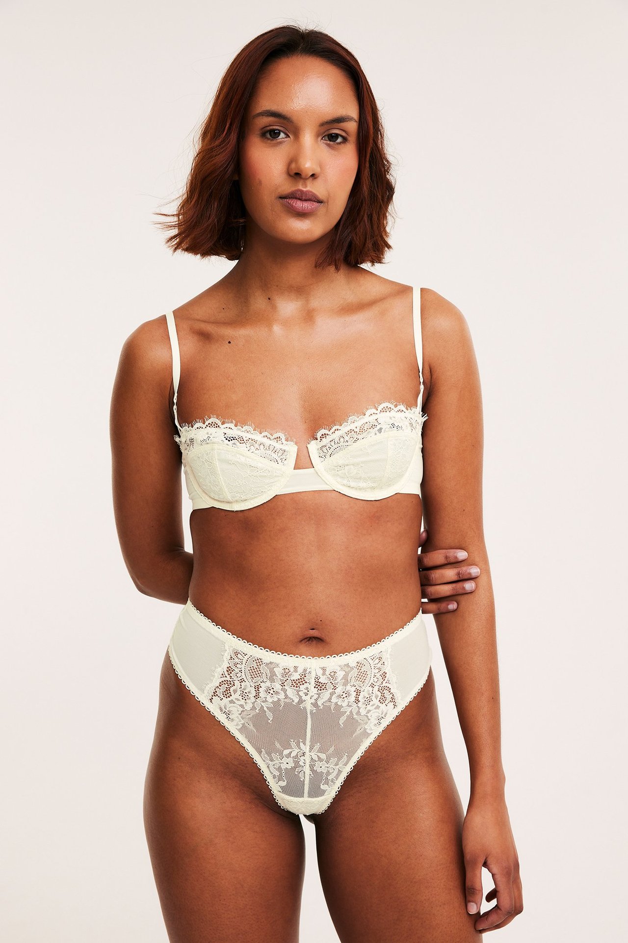 Naisen etunäkymä yllään luonnonvalkoiset pitsistringit ja yhteensopivat pitsirintaliivit.