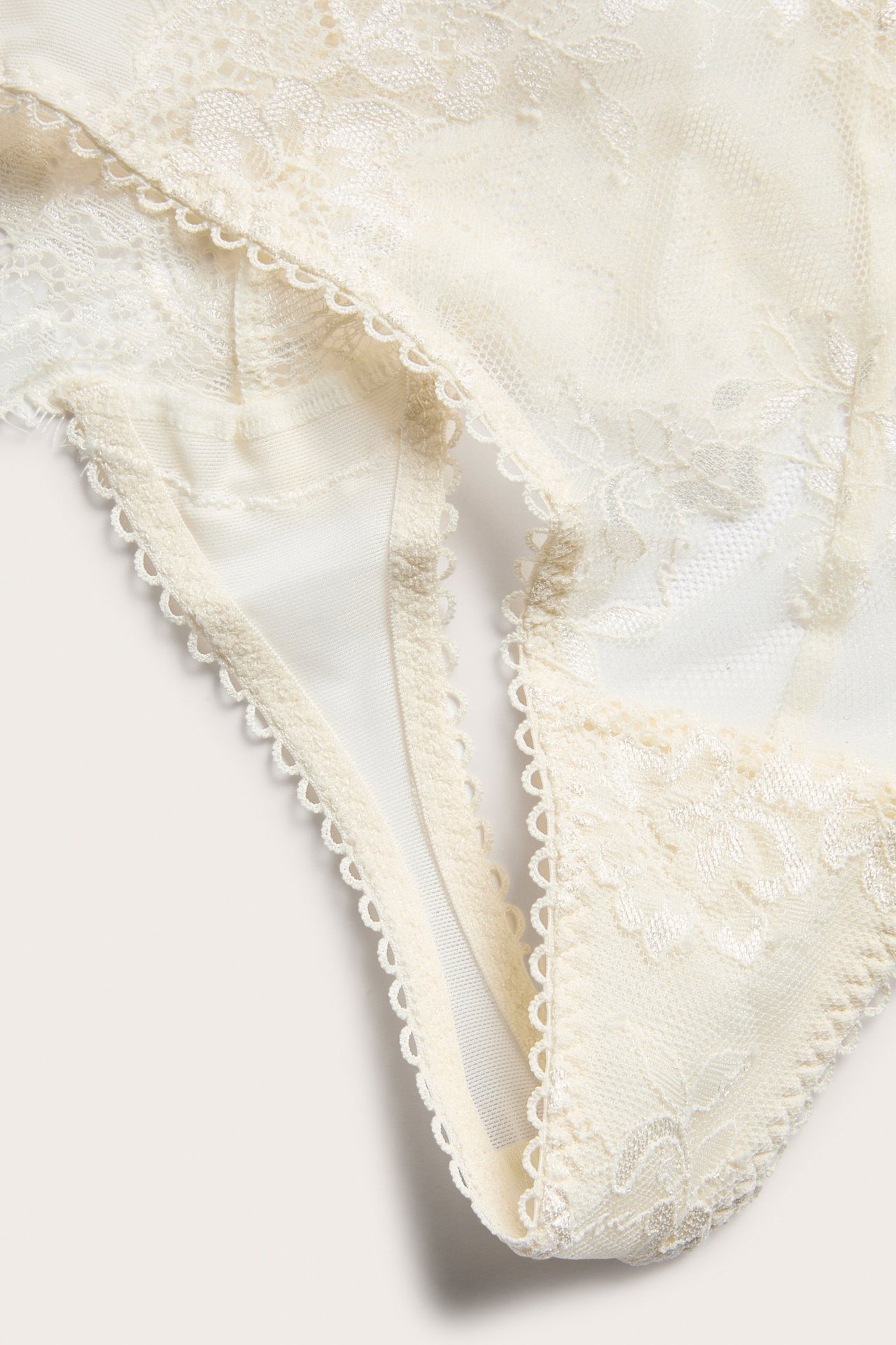 Zbliżenie na koronkowe stringi w kolorze złamanej bieli z delikatnymi falbankami.