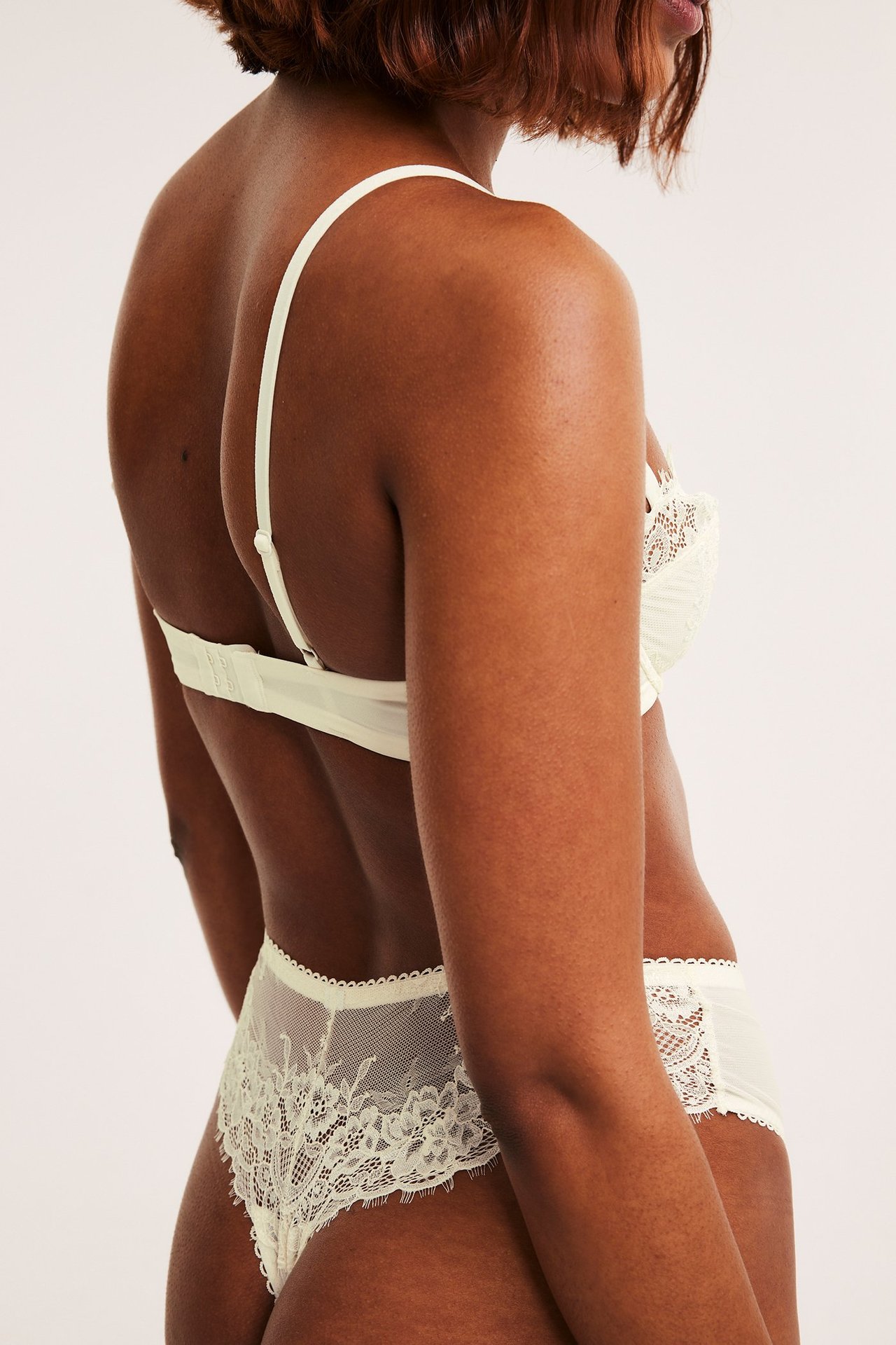 Naisen selkäpuolelta: luonnonvalkoiset pitsstringit ja yhteensopivat luonnonvalkoiset rintaliivit.