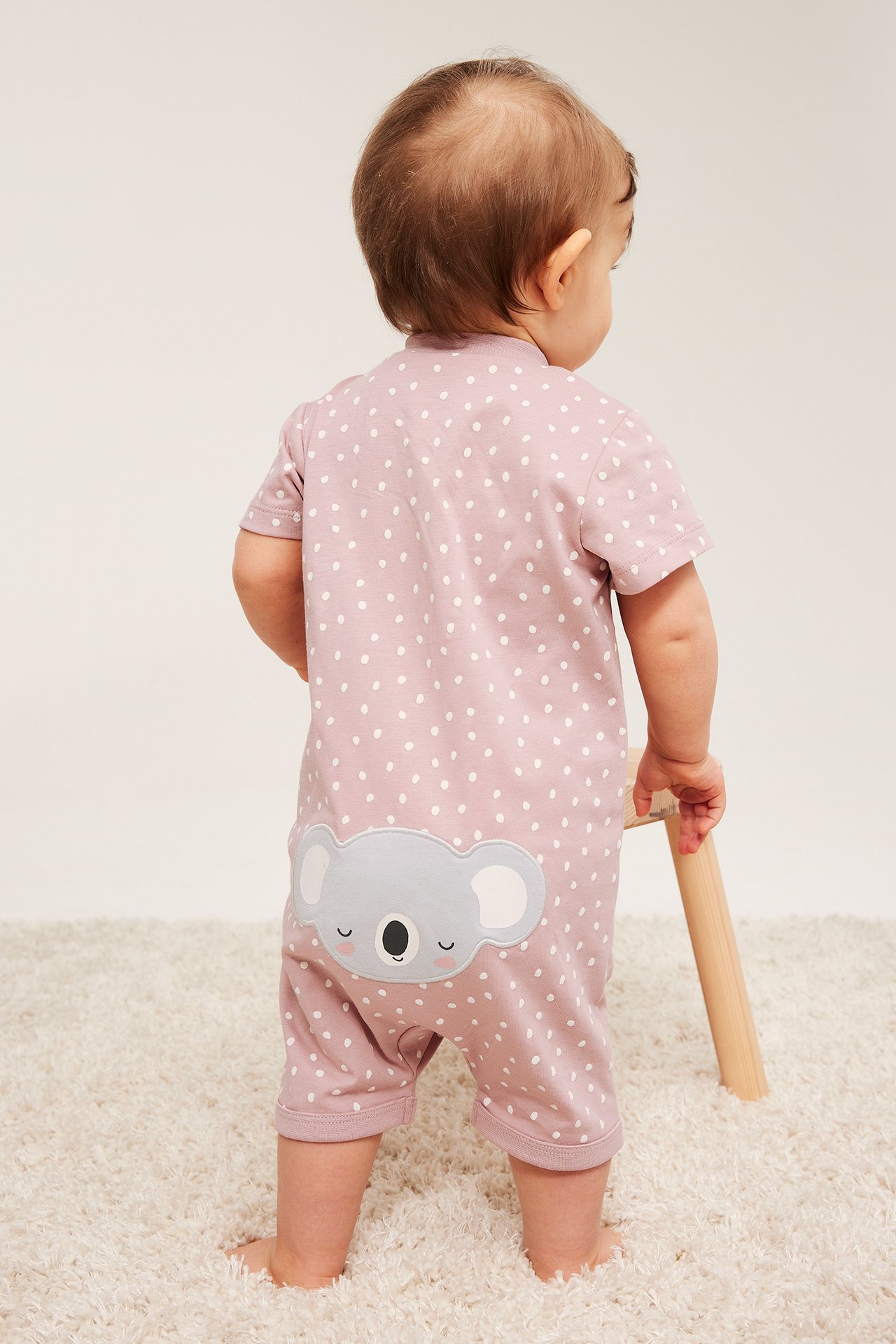 Vaaleanpunainen pilkullinen lyhythihainen haalari koala-applikaatiolla vauvan päällä, takakuva.