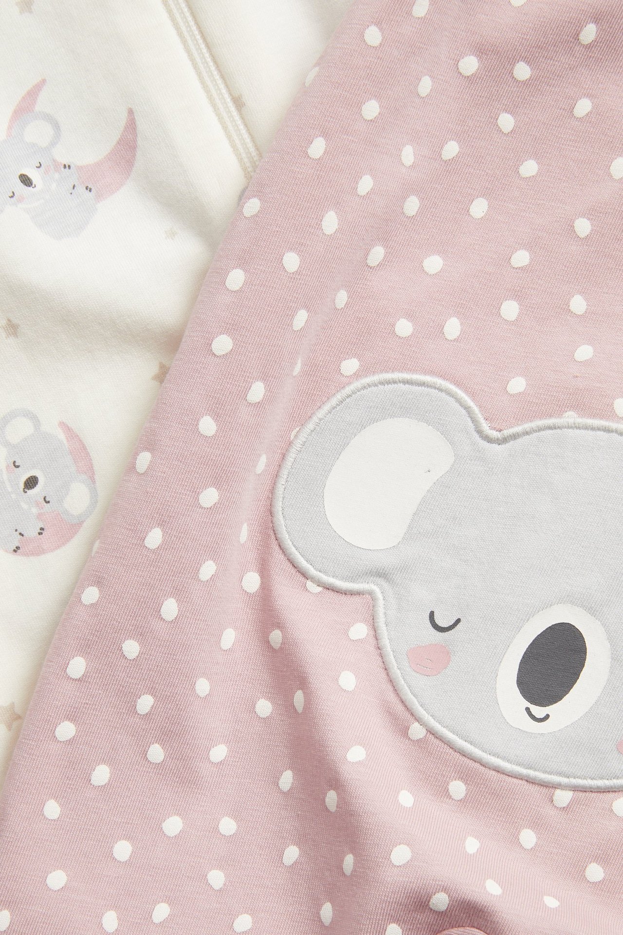 Lähikuva kahdesta vauvanpotkupuvusta: vaaleanpunainen pilkullinen koala-applikaatiolla ja luonnonvalkoinen koalakuvioinen.