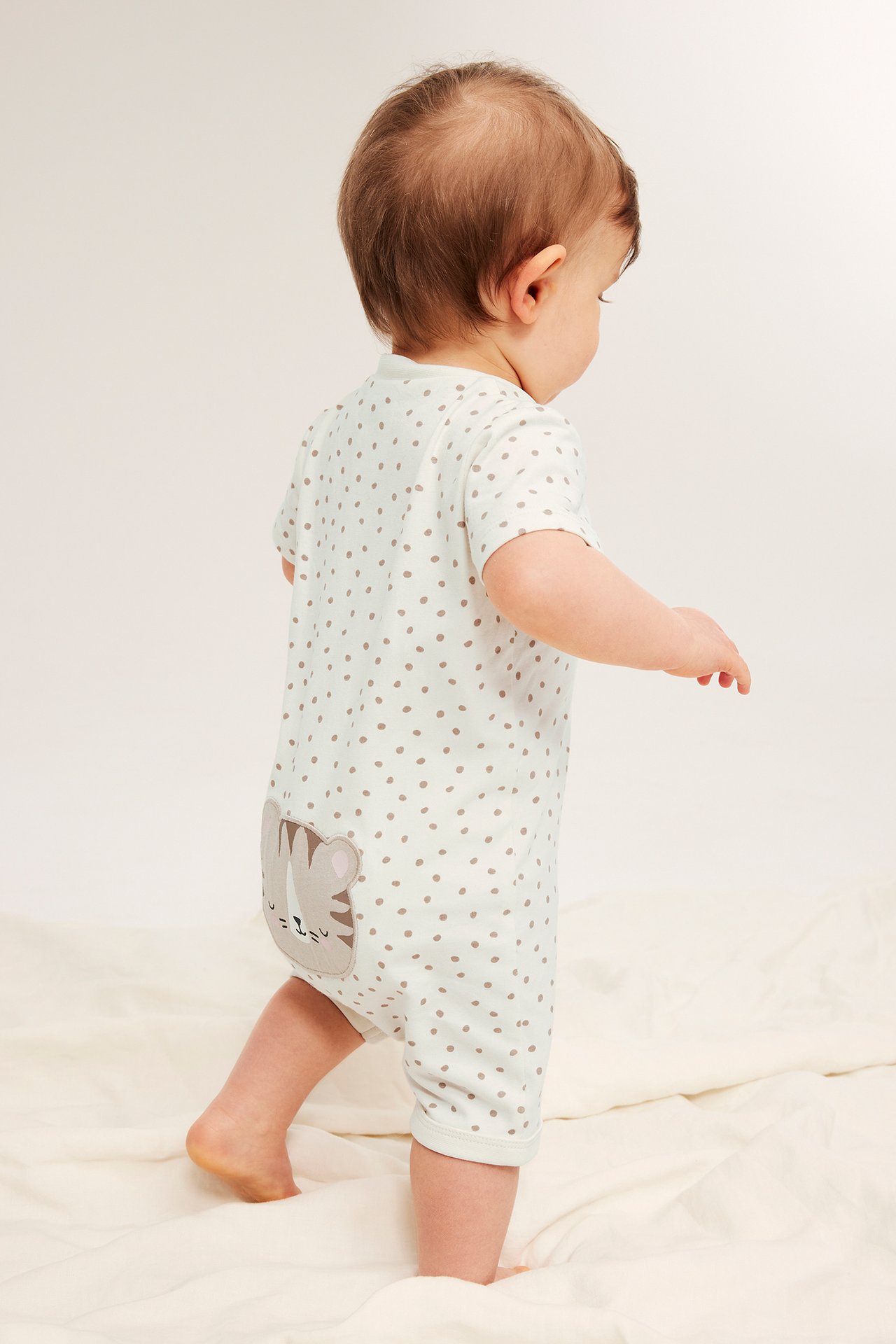 Vauvan takanäkymä: beige lyhythihainen pilkullinen romper harmaalla tiikerisovelluksella.