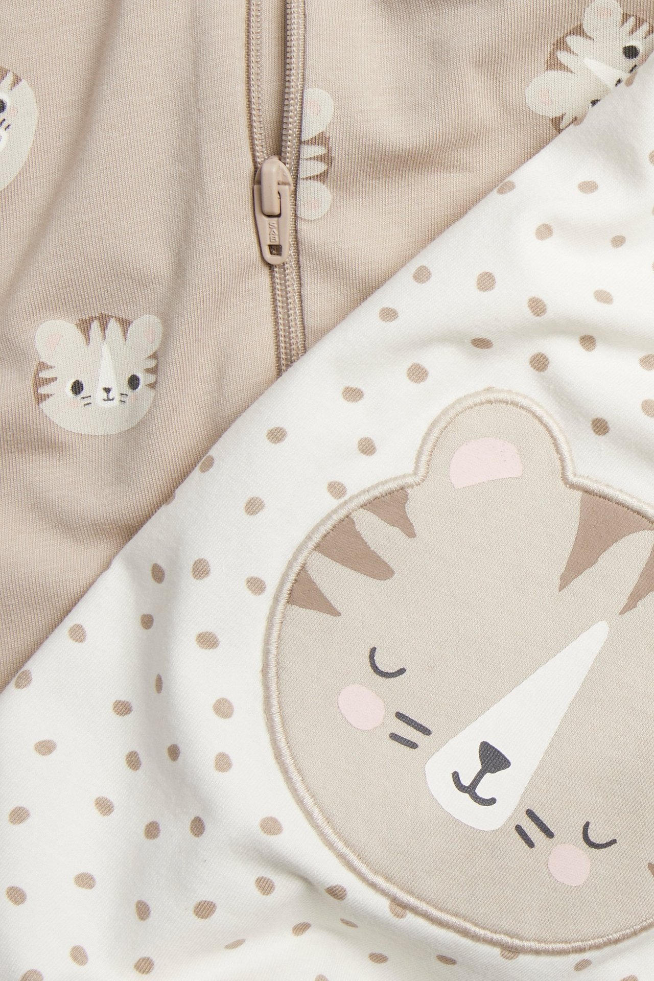 Vauvan kaksi lyhythihaista romperia: beige tiikerikuviolla ja vetoketjulla, pilkullinen tiikerisovelluksella.