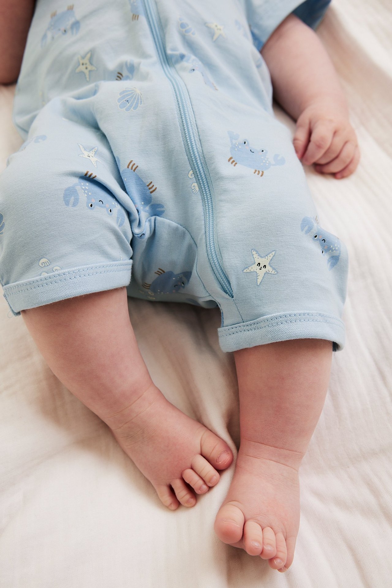 Zbliżenie: Niemowlę w jasnoniebieskim, krótkim pajacyku w kraby i rozgwiazdy, z zamkiem błyskawicznym jednokierunkowym.