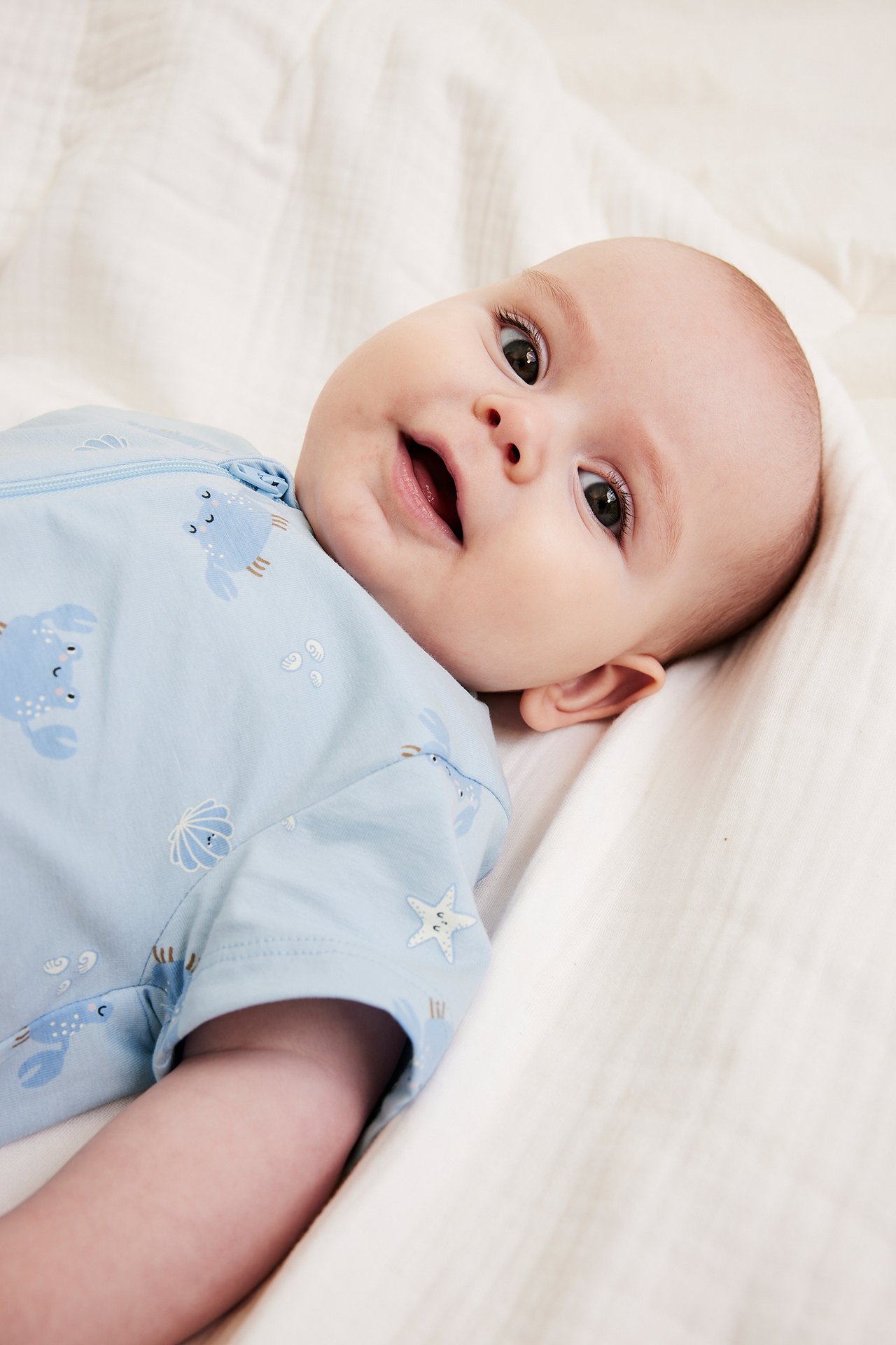 Zbliżenie dziecka w jasnoniebieskim krótkim pajacyku z wzorem krabów i muszli, zapinanym na zamek.