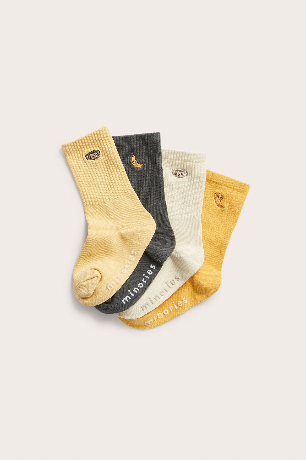 Edestä, neljä ribattua puuvillasukkaa keltaista, harmaata ja luonnonvalkoista, apina- tai banaanikirjonnalla.