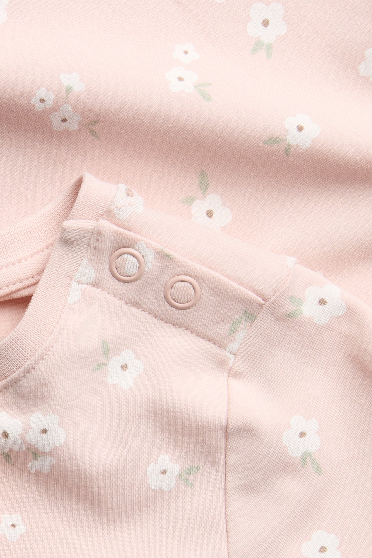 Nærbilde av en rosa kortermet babybody med hvitt blomstermønster og trykknapper på skulderen.