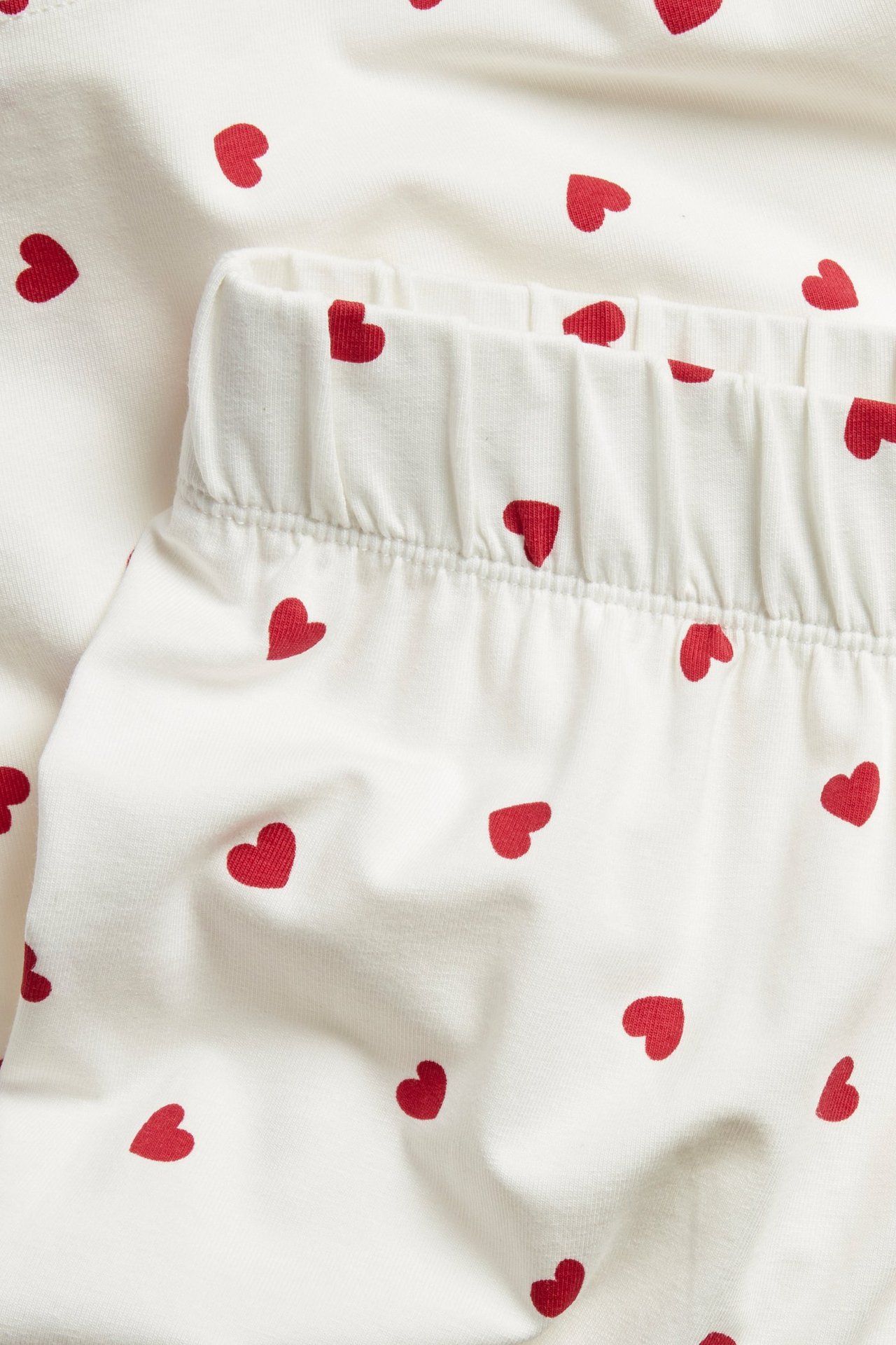Närbild på offwhite pyjamasshorts med rött hjärtmönster, med resår i midjan.