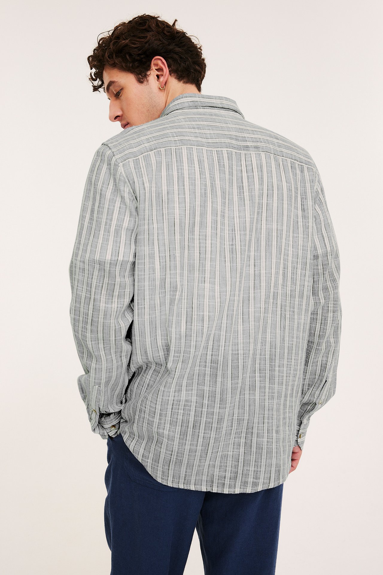 Mann, bakfra, i en blåstripet bomullsskjorte med struktur og mørkeblå bukser.