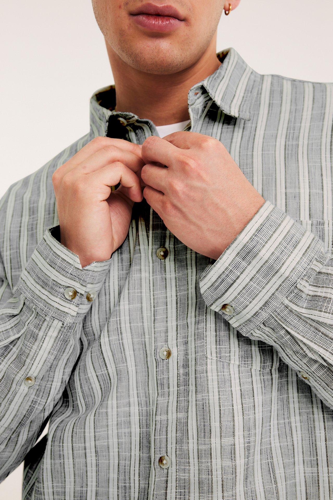 Nærbilde av en mann som knepper en lysegrå og hvitstripet bomullsskjorte med struktur.