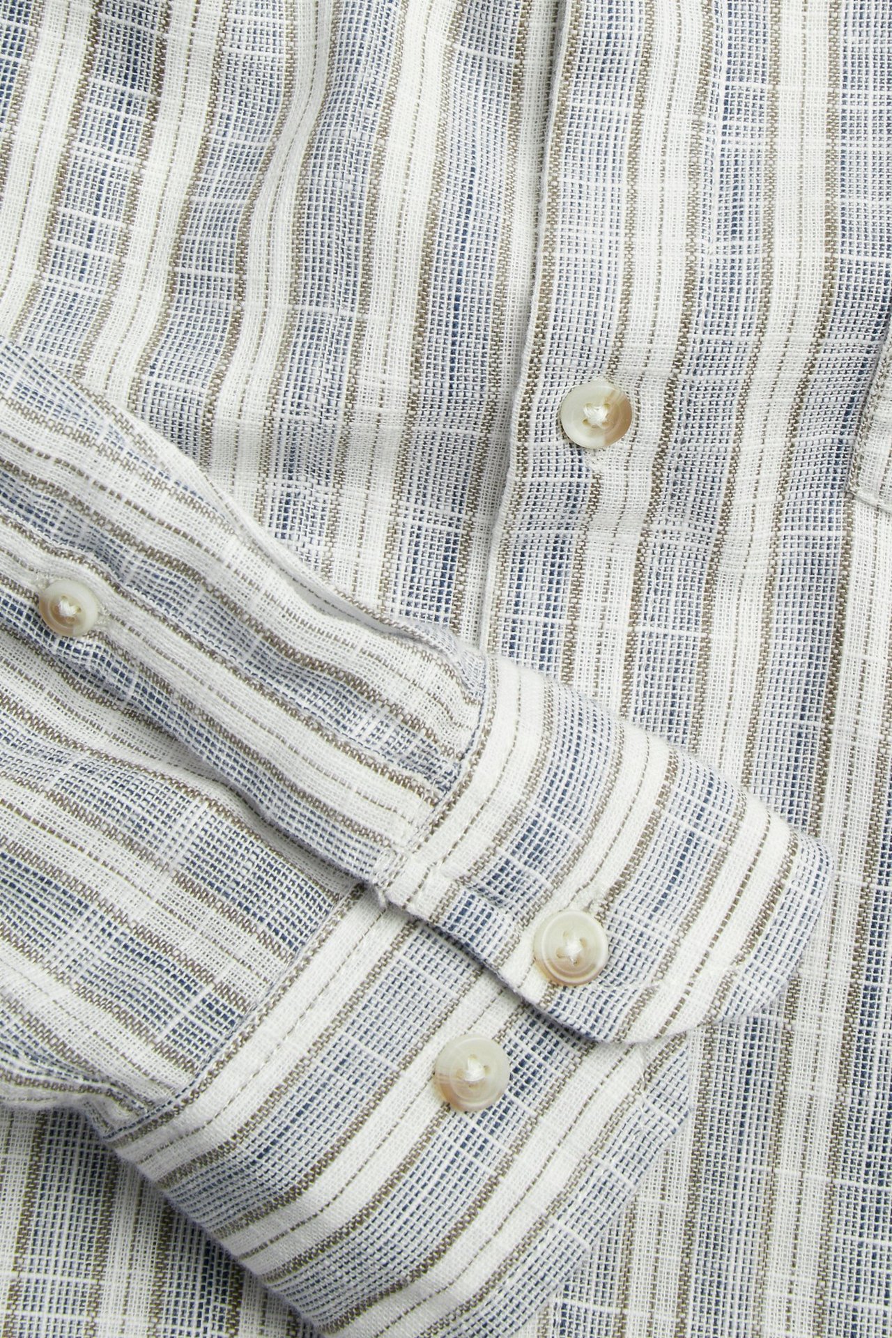 Närbild av en blå- och vitrandig bomullsskjorta med struktur, visar knappar på knappslå och manschett.