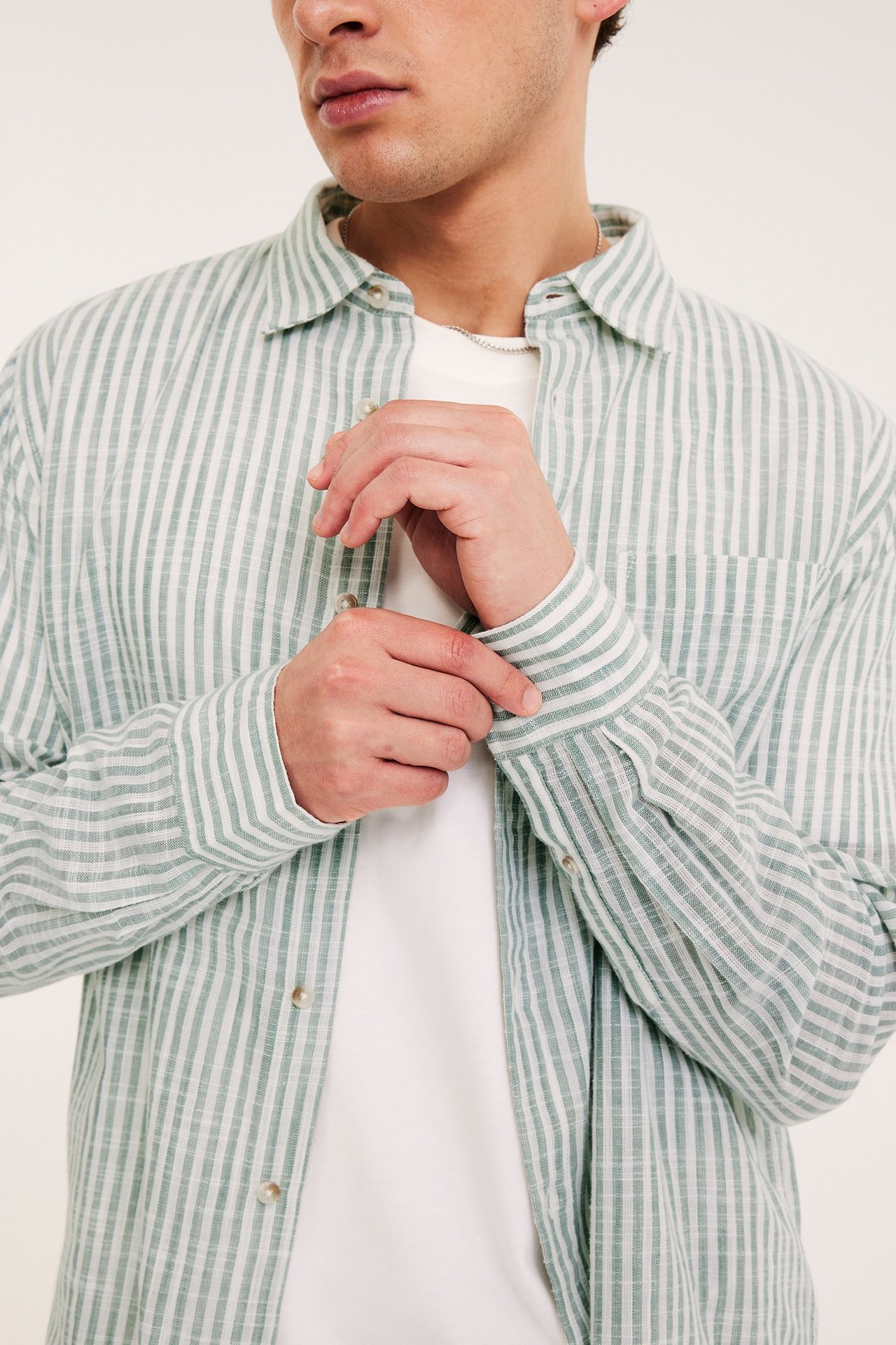 Nærbilde forfra: Mann i lys grønn stripete bomullsskjorte over hvit t-skjorte, justerer mansjetten.