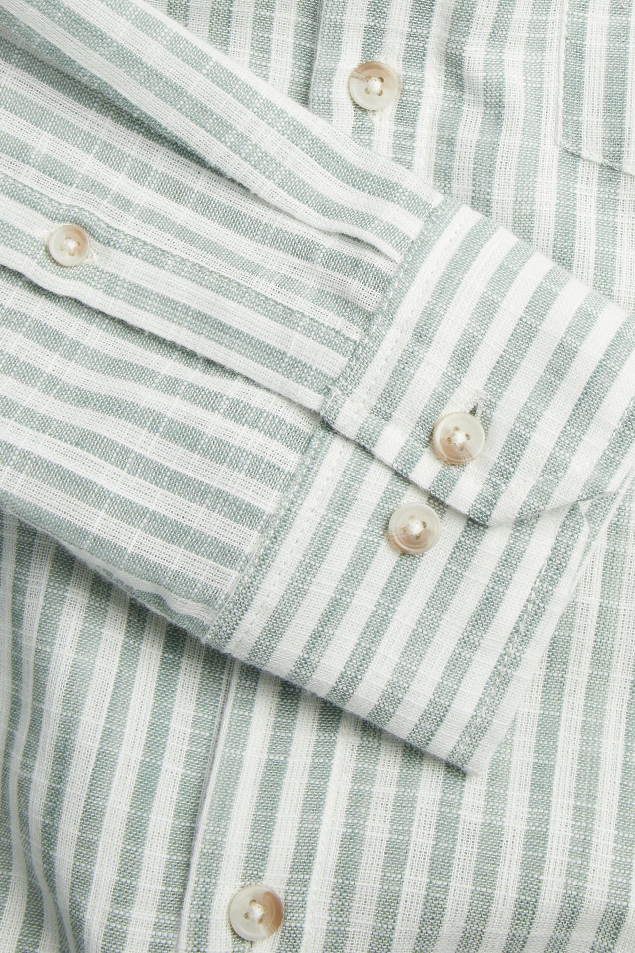 Närbild av en ljusgrön och vit randig bomullsskjorta med struktur, som visar en manschett med två knappar.