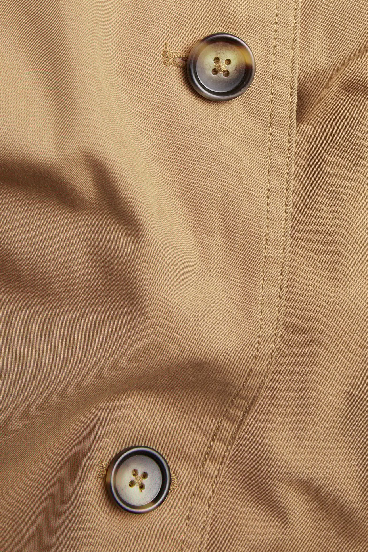 Zbliżenie beżowego trenczu z dwoma brązowymi, cętkowanymi guzikami.