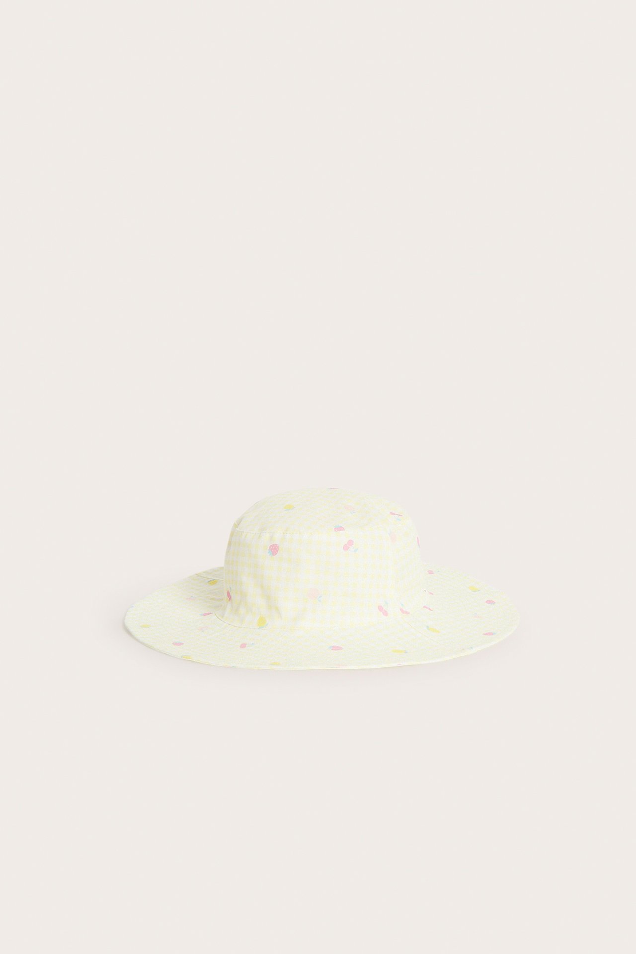 Framifrån, en rutig solhatt för barn i ljusgul bomullstwill med färgglatt frukt- och grönsaksmönster.