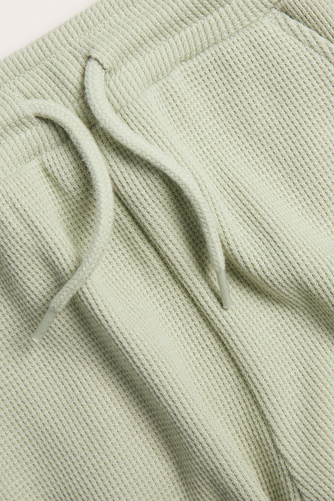 Nærbilde av lysegrønne vaffelstrikkede bomullsshorts med synlig snøring.