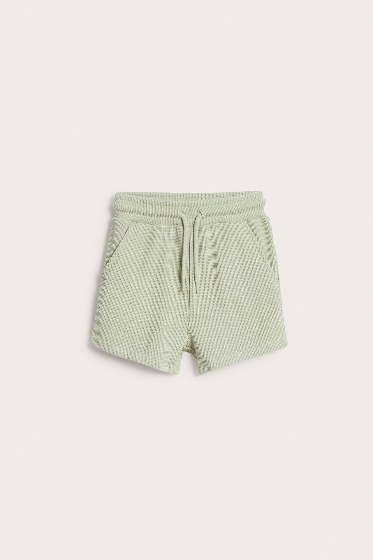 Frontvisning av lysegrønne vaffelstrikkede shorts med elastisk snøring i midjen og to frontlommer.