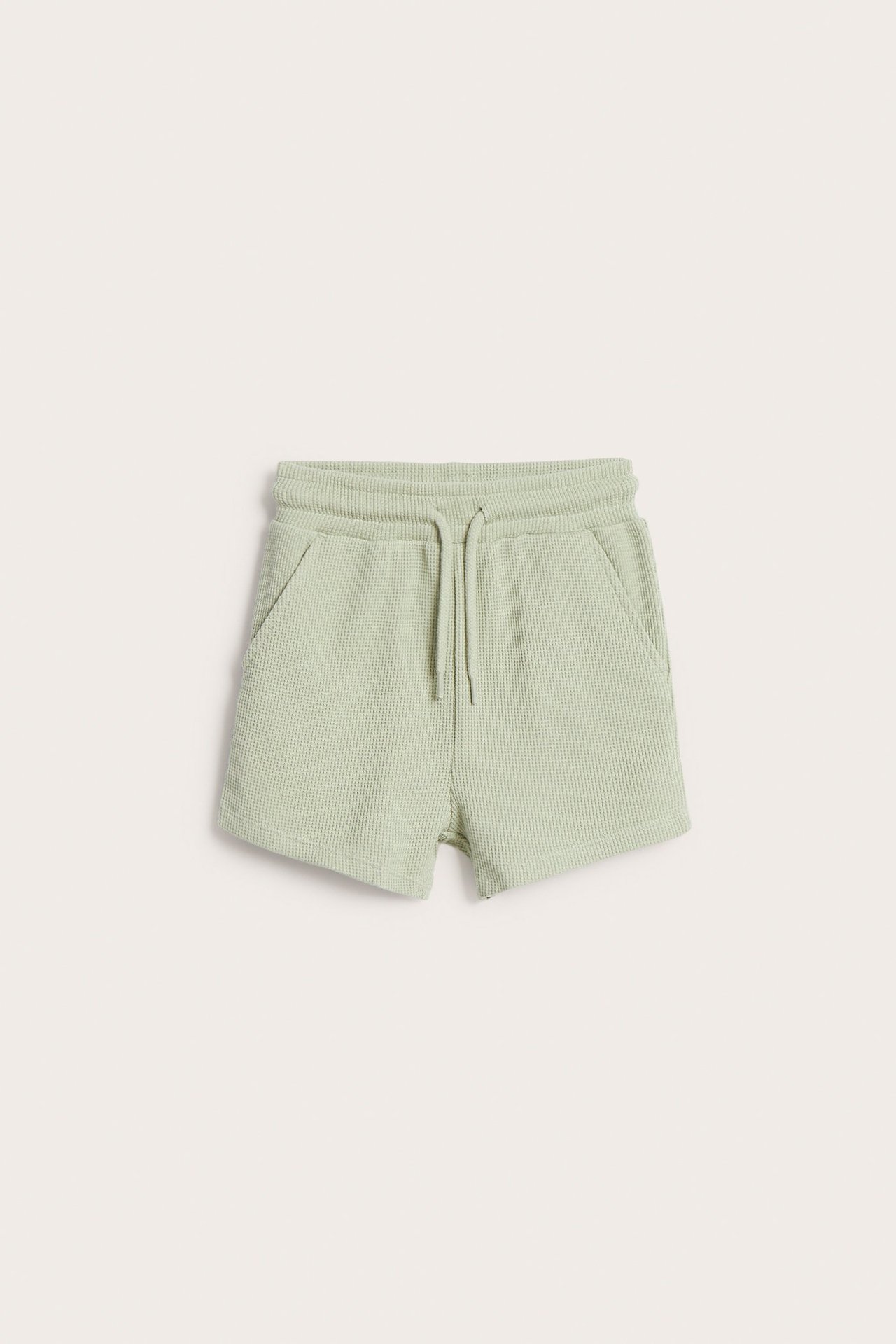 Frontvisning av lysegrønne vaffelstrikkede shorts med elastisk snøring i midjen og to frontlommer.