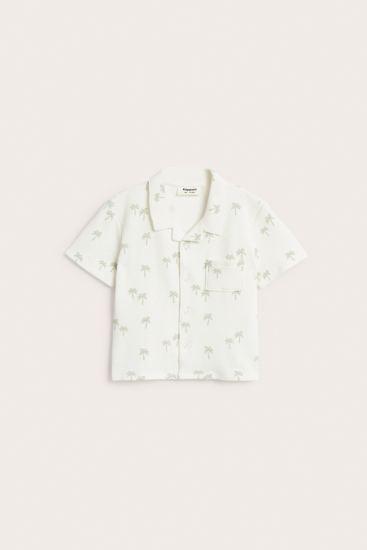 Frontvisning av en offwhite kortermet vaffelskjorte for baby med grønt palmemønster og lomme.