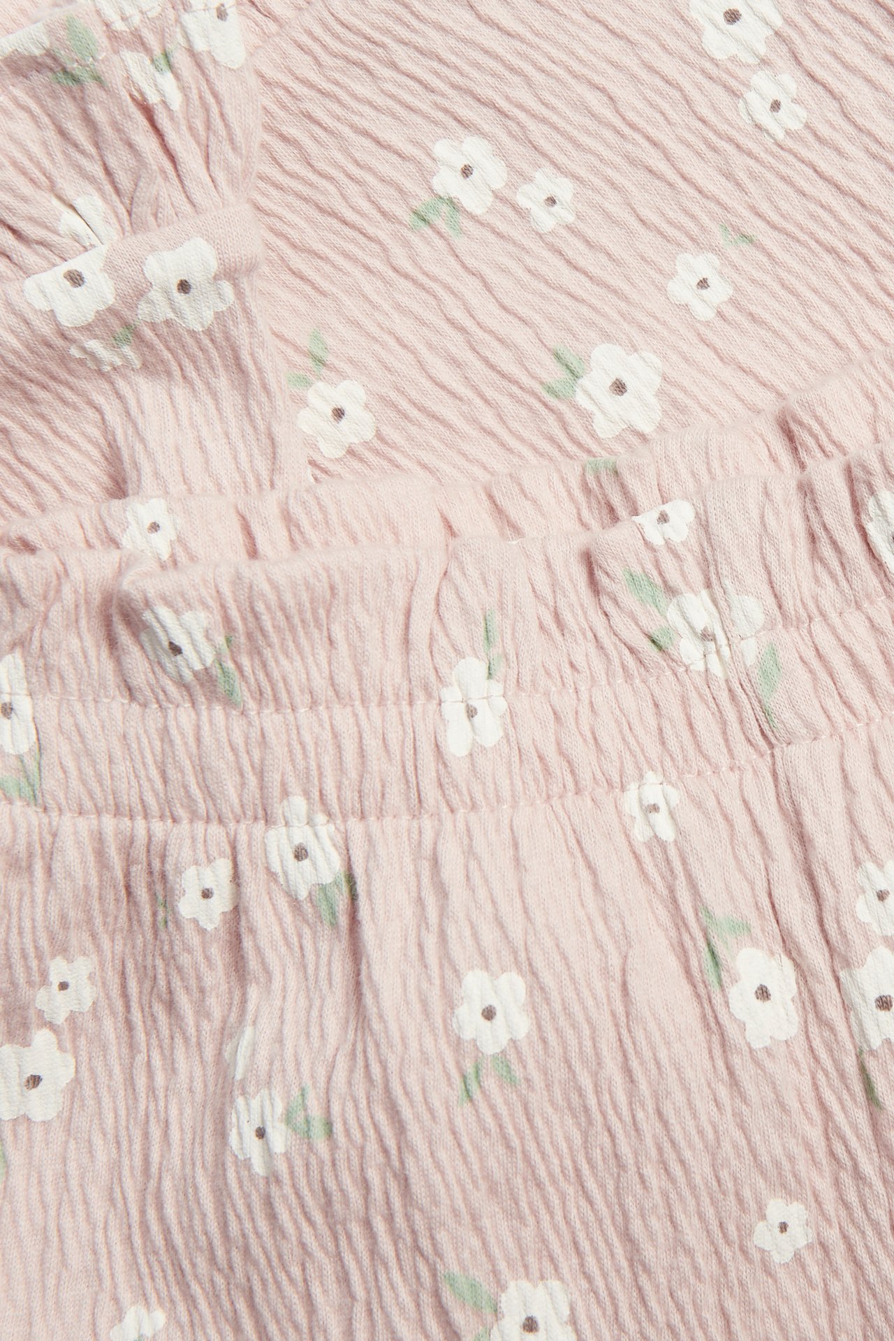 Nærbilde av rosa babybukser i bomullskrepp med elastisk volangmidje og blomstermønster.