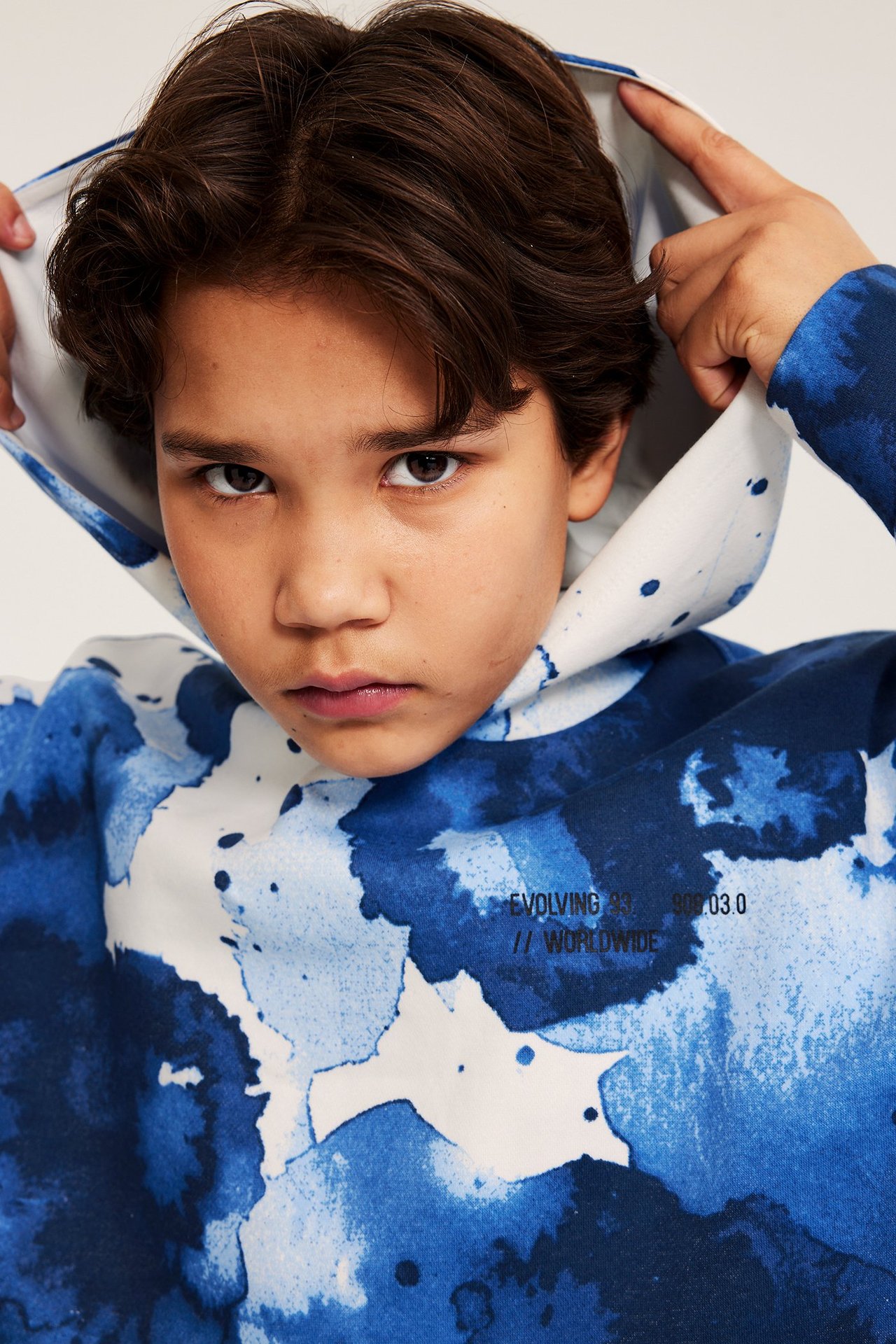 Nærbilde forfra av et barn i en offwhite og blåmønstret hettegenser, som trekker opp hetten.