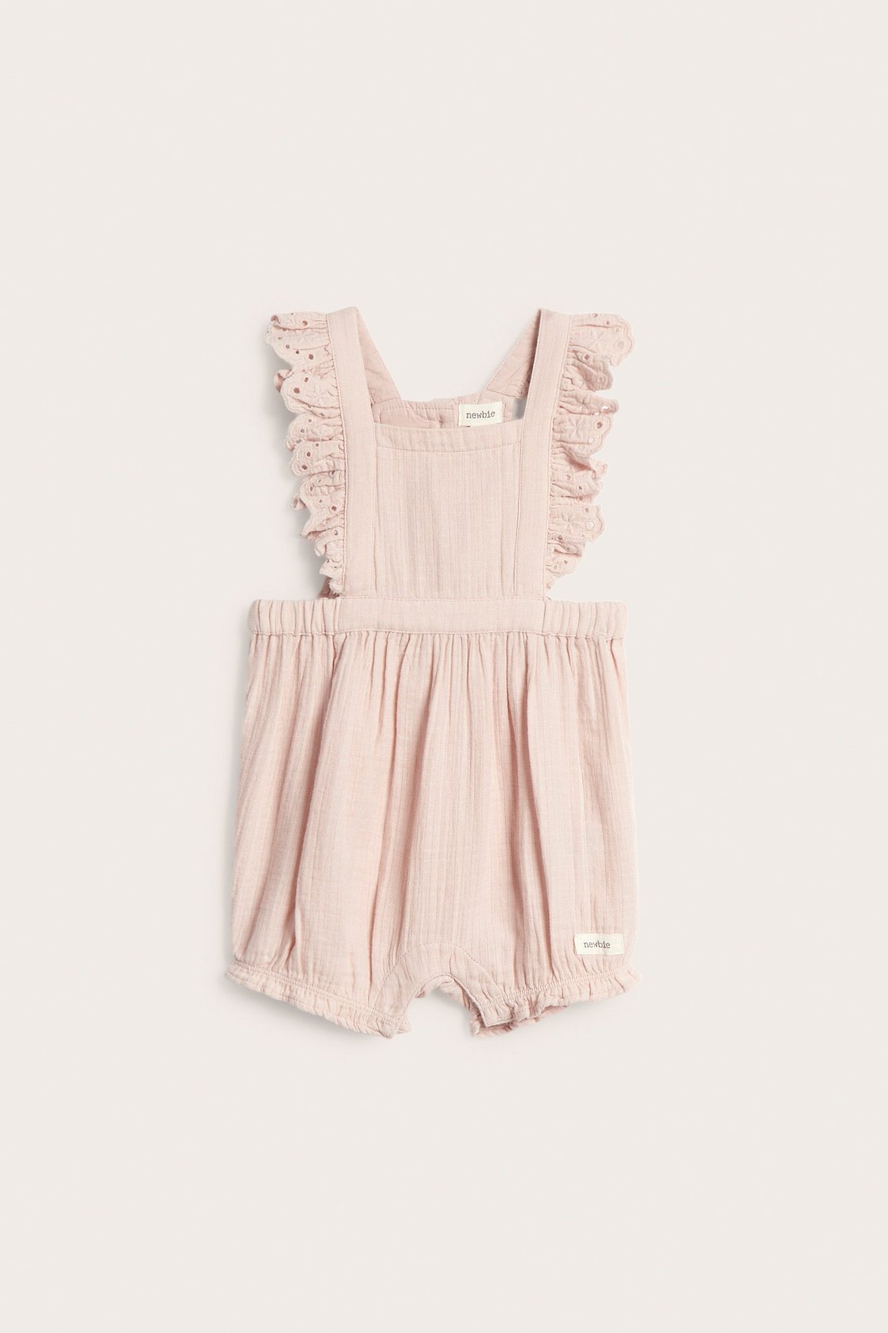 Frontvisning av lyserosa vevde babyselebukser med volangblondestropper og strikk i bena.