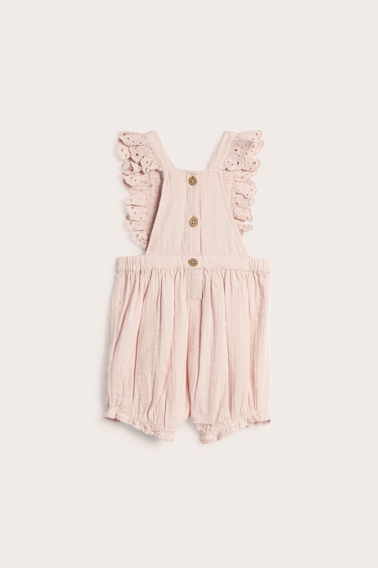 Forfra: babyens lyse rosa bomullsshorts med blondevolanger på stroppene og treknapper.