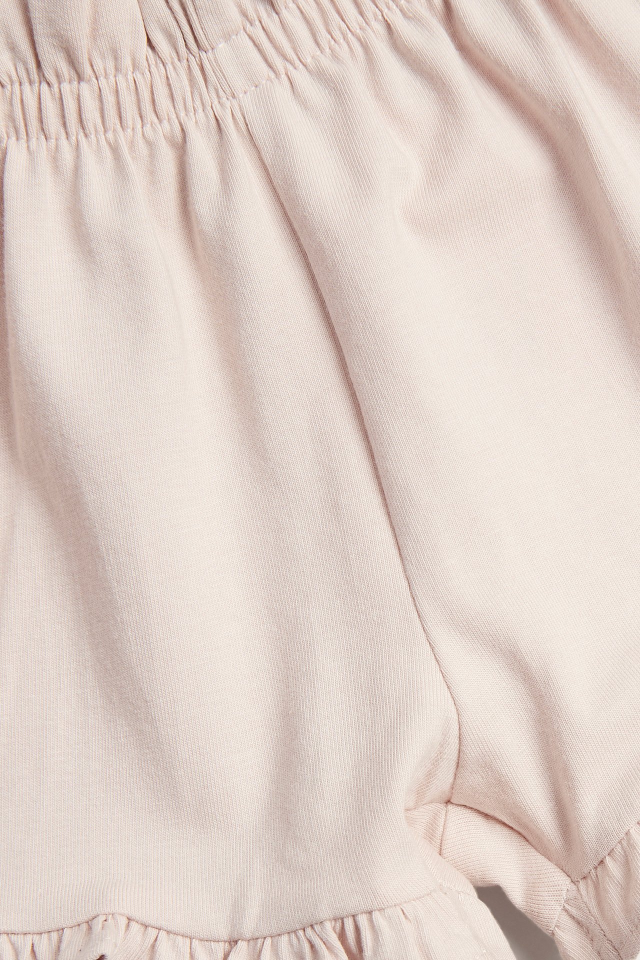 Lähikuva vaaleanpunaisista vauvan jersey-shortseista, joissa kuminauhavvyötärö ja röyhelöt lahkeensuissa.