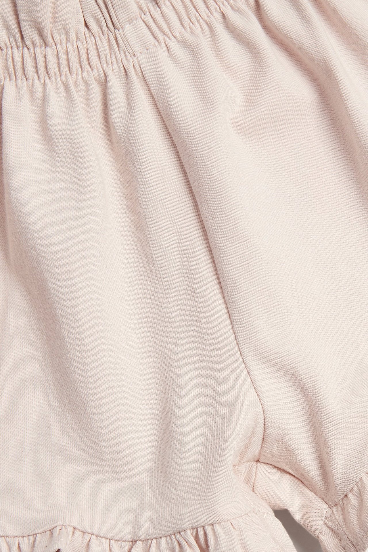 Nærbilde av lyserosa jersey-babyshorts med elastisk midje og rysjer ved benåpningene.