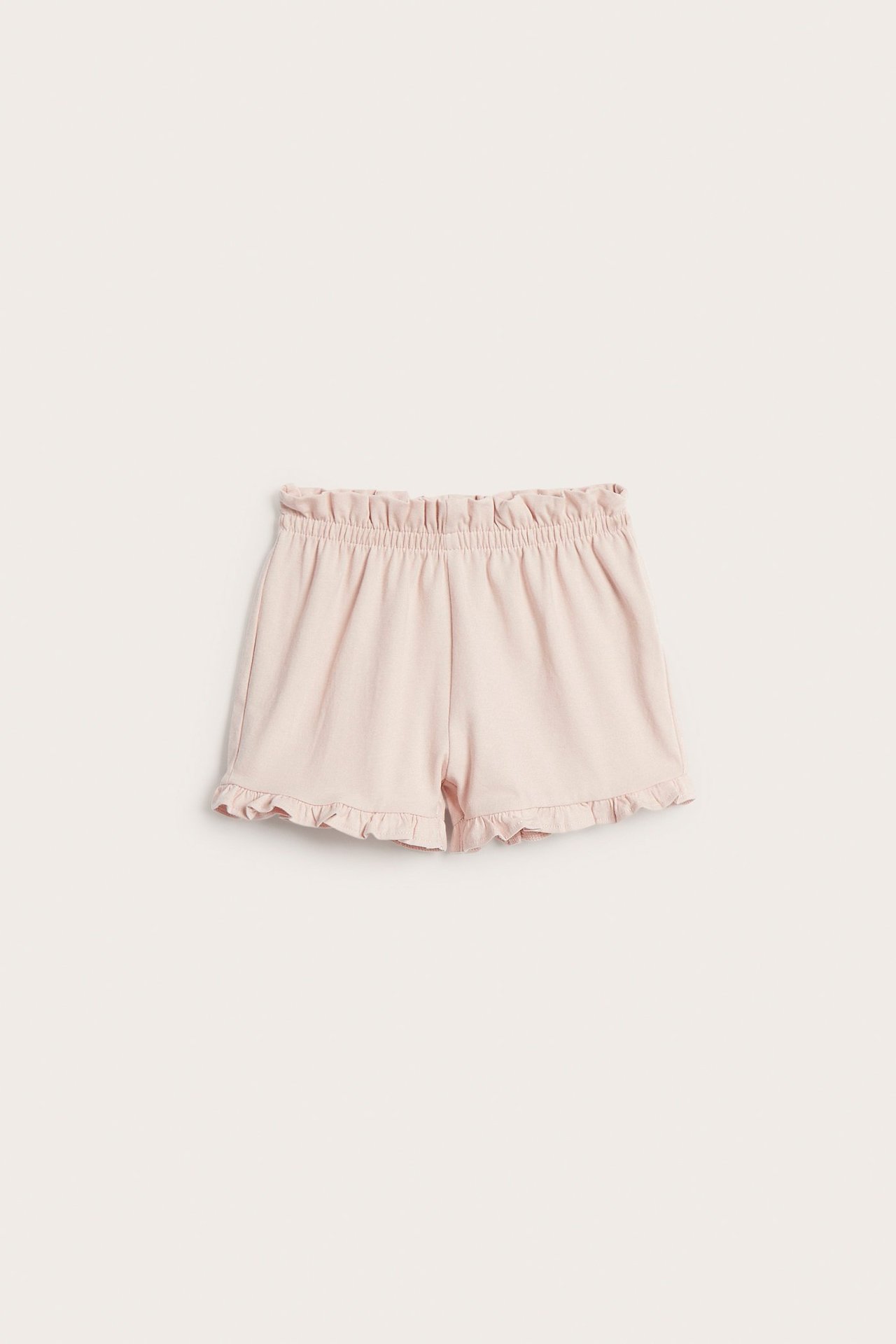 Framsiden av ensfargede lyserosa babyshorts med rynket elastisk midje og volangkant ved benåpningene.