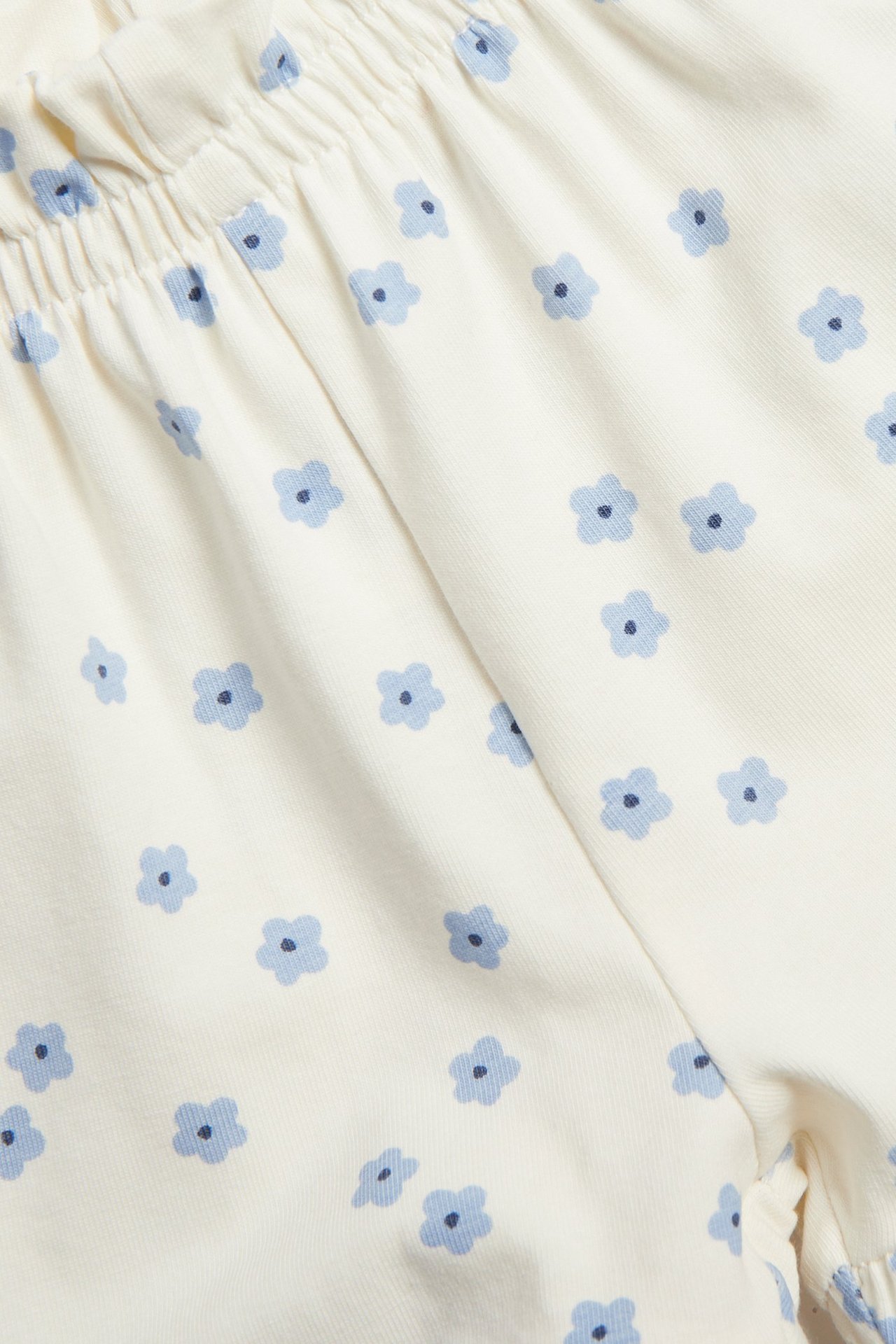 Nærbilde av offwhite baby shorts med blått blomstermønster, elastisk volangkant i livet.