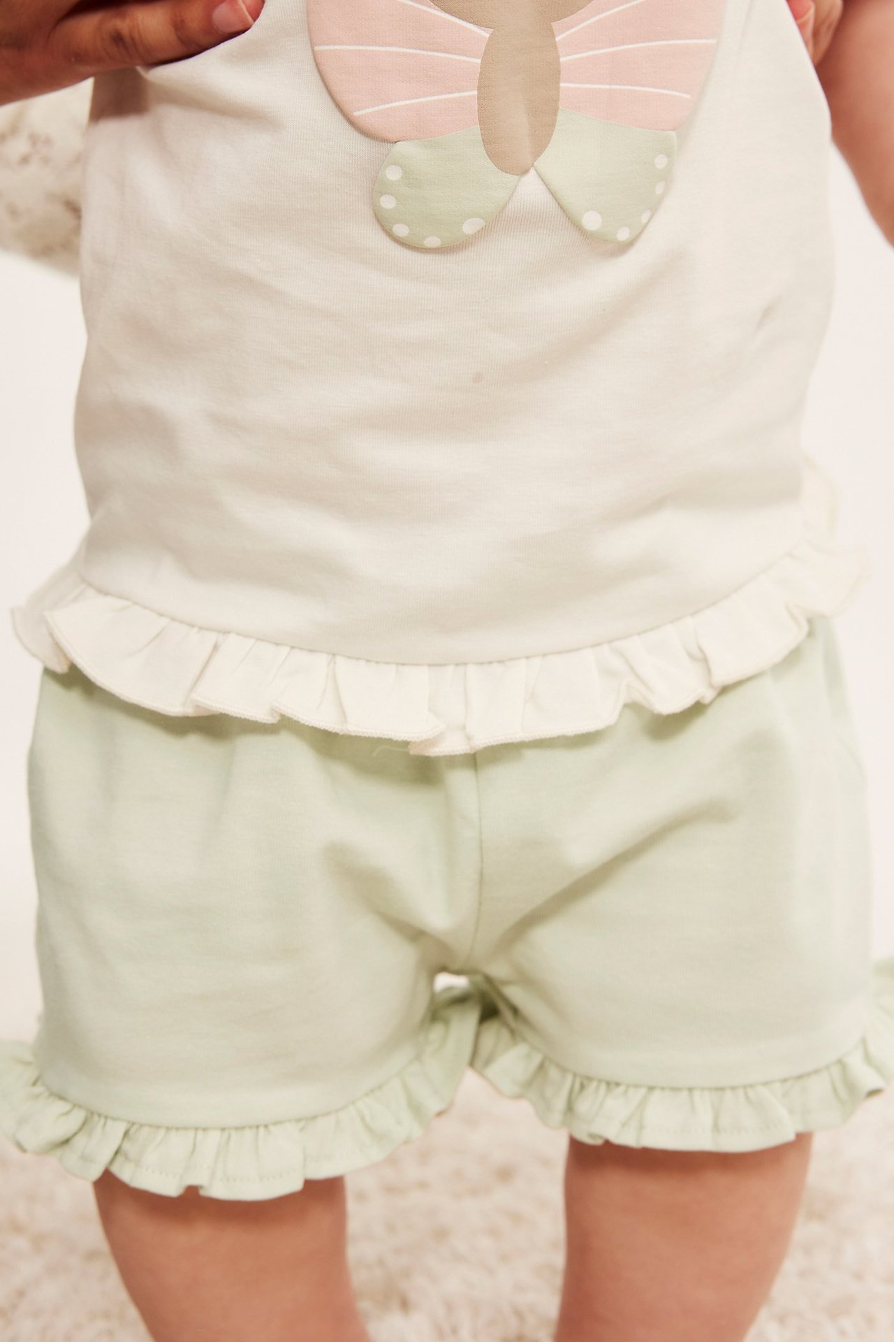 Edestä: Vauva yllään vaaleanvihreät rypytetyt jersey-shortsit ja vaalea toppi, jossa on applikointi.