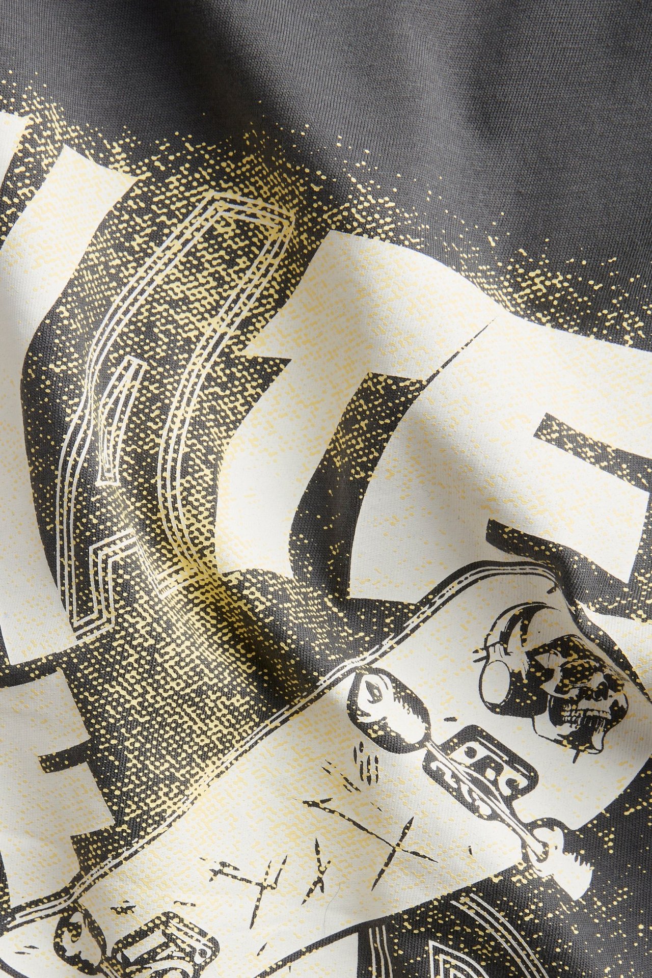 Zbliżenie czarnego, bawełnianego T-shirtu z biało-żółtym nadrukiem podwójnego efektu: tekst, deskorolka, czaszka.