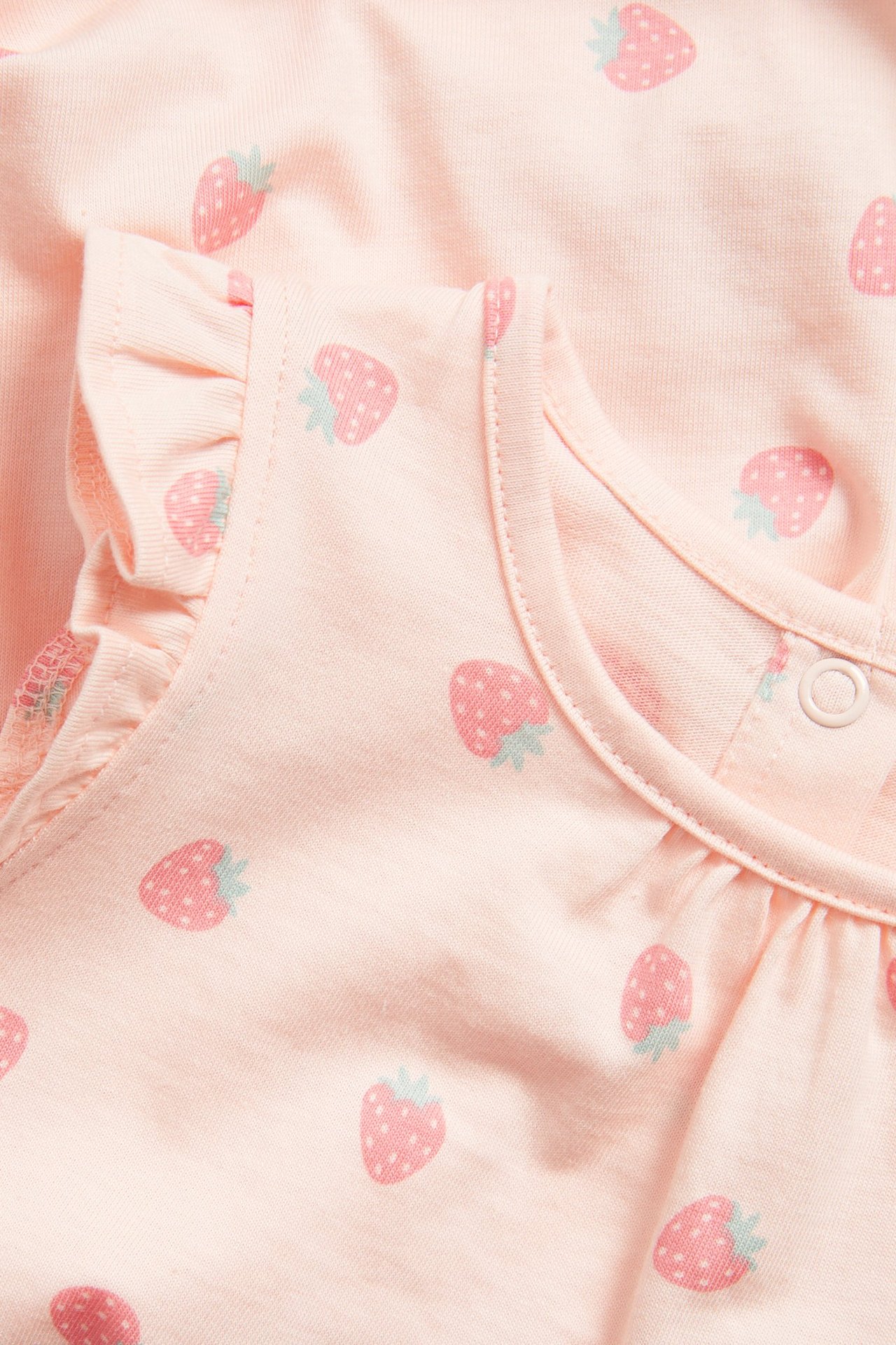 Lähikuva vauvan vaaleanpunaisesta puuvillabodysta mansikkakuviolla, röyhelöhihoilla ja olkapäänepparilla.