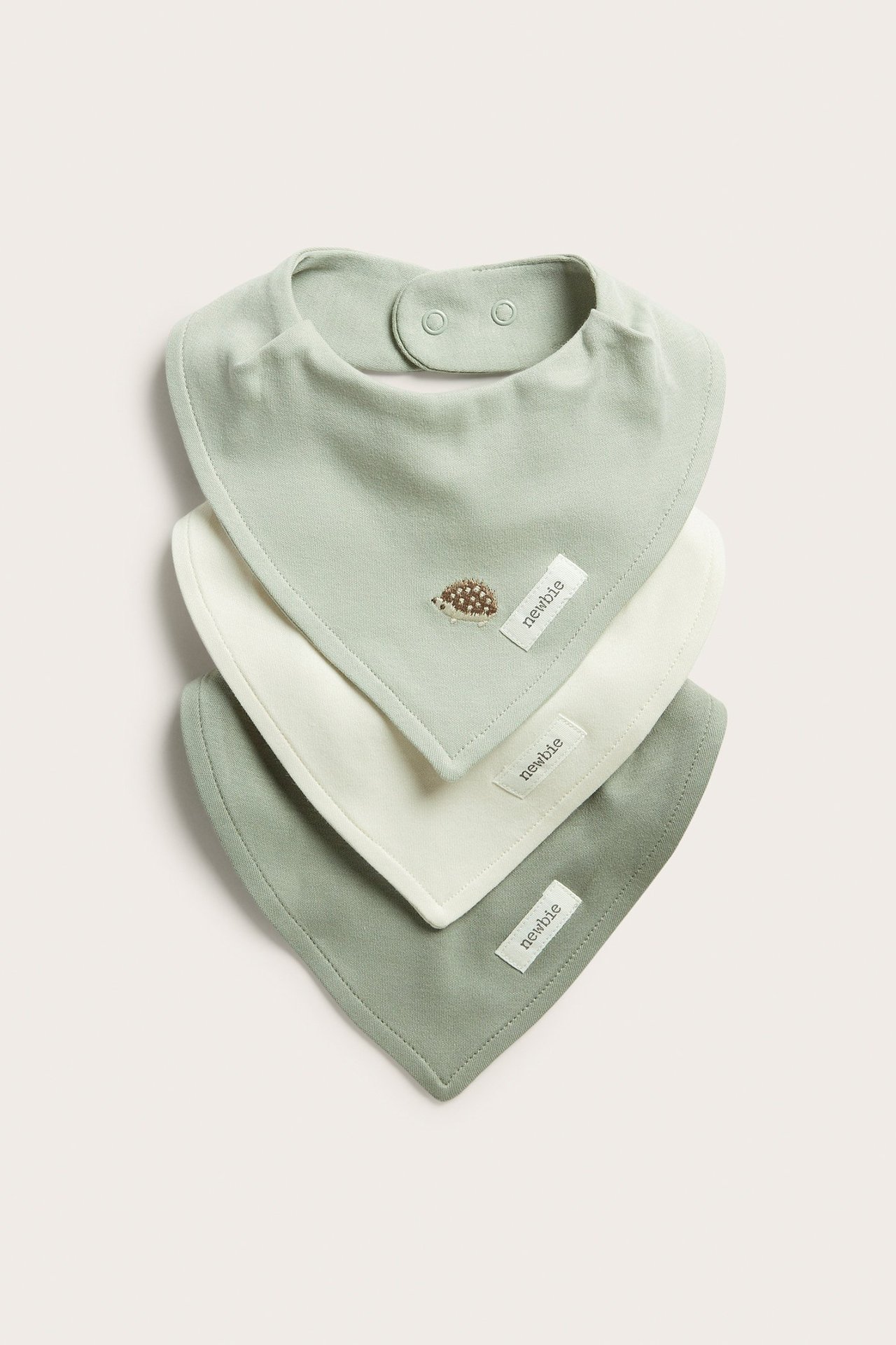 Edestä: Kolme pehmeää puuvillaista ruokalappua. Vaaleanvihreä siilikirjonnalla, kerma ja tummanvihreä. Painonappikiinnitys.