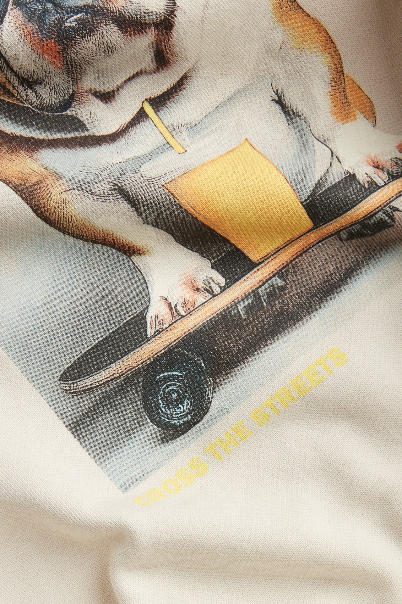 Närbild på en ljusbeige sweatshirt i bomull med fronttryck av en bulldog på skateboard.