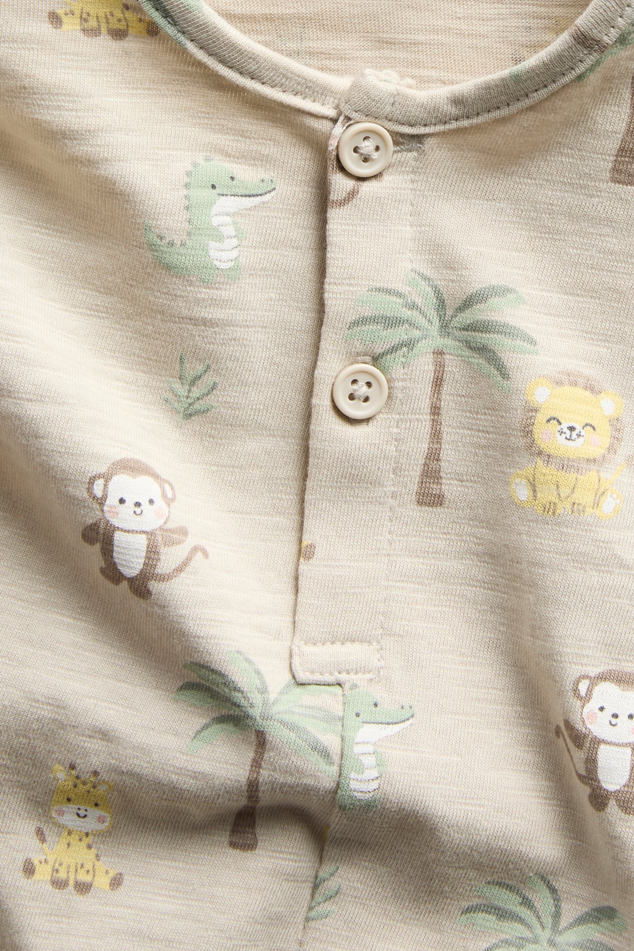 Nærbilde av en beige bomullsslub-romper for baby med dyremønster og knapper foran.