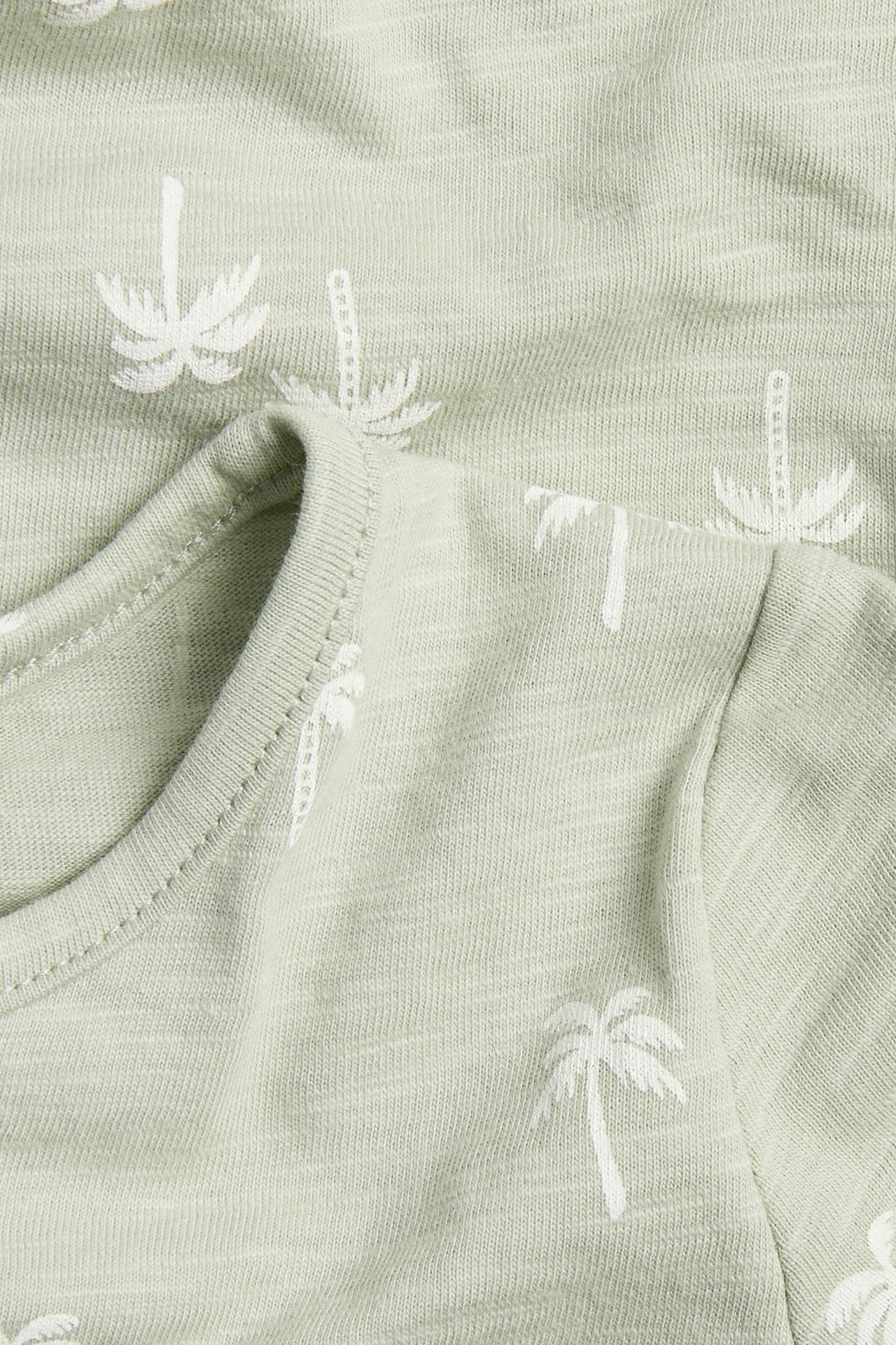 Nærbilde av en babys lysegrønne bomullsromper med et heldekkende hvitt palmemønster.