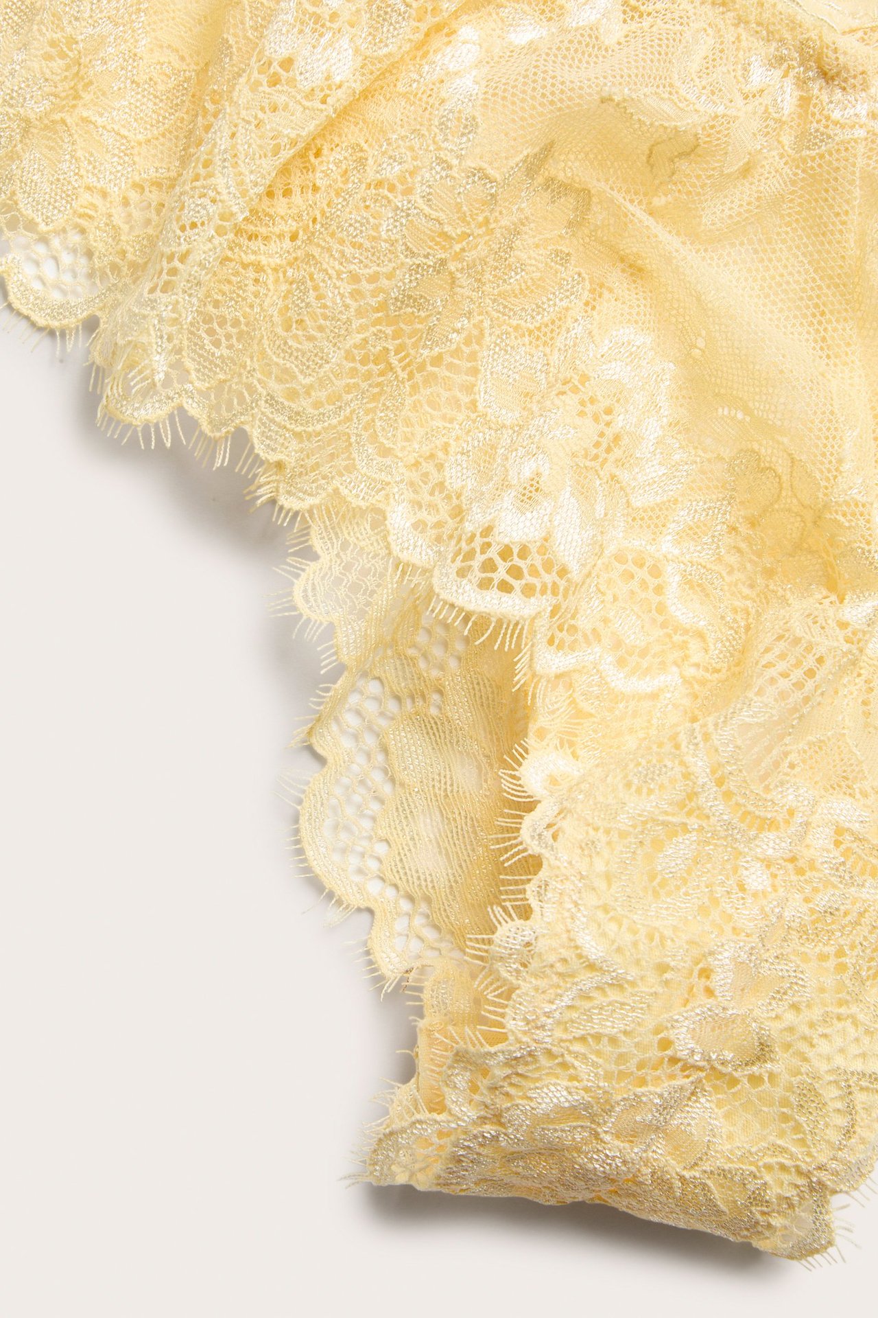 Zbliżenie na jasne żółte majtki typu cheeky z delikatnej koronki w kwiatowy wzór.
