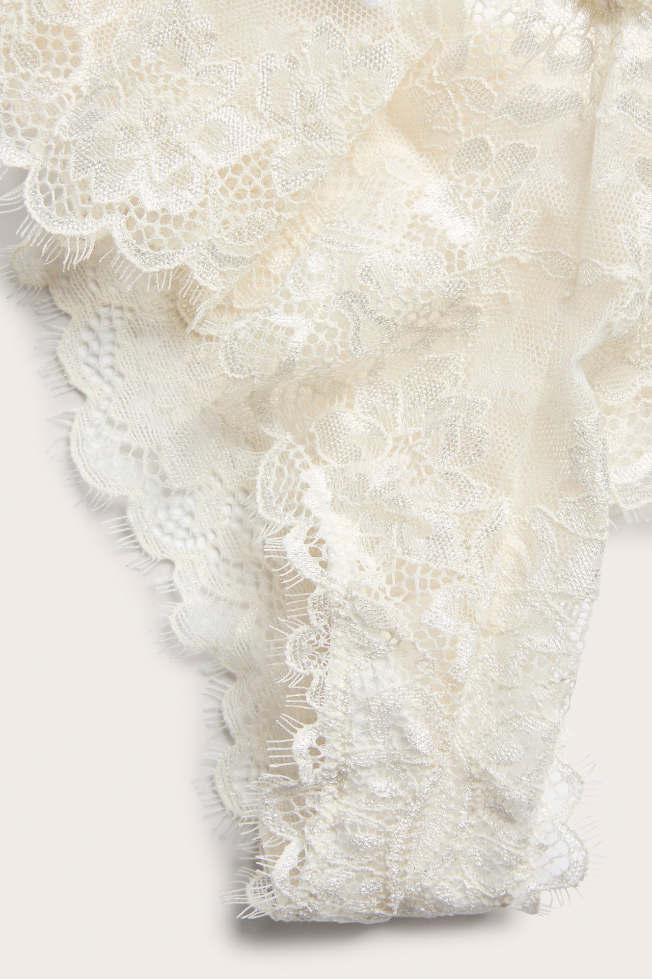 Närbild av en offwhite spets-cheeky trosa med intrikata blommönster längs den vågiga kanten.