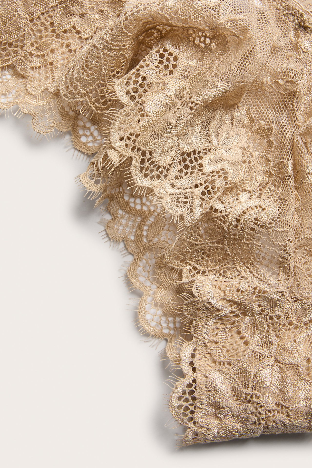 Lähikuva beigeistä pitsisistä cheeky-alushousuista, joissa kukkakuvio ja aaltoileva reuna.